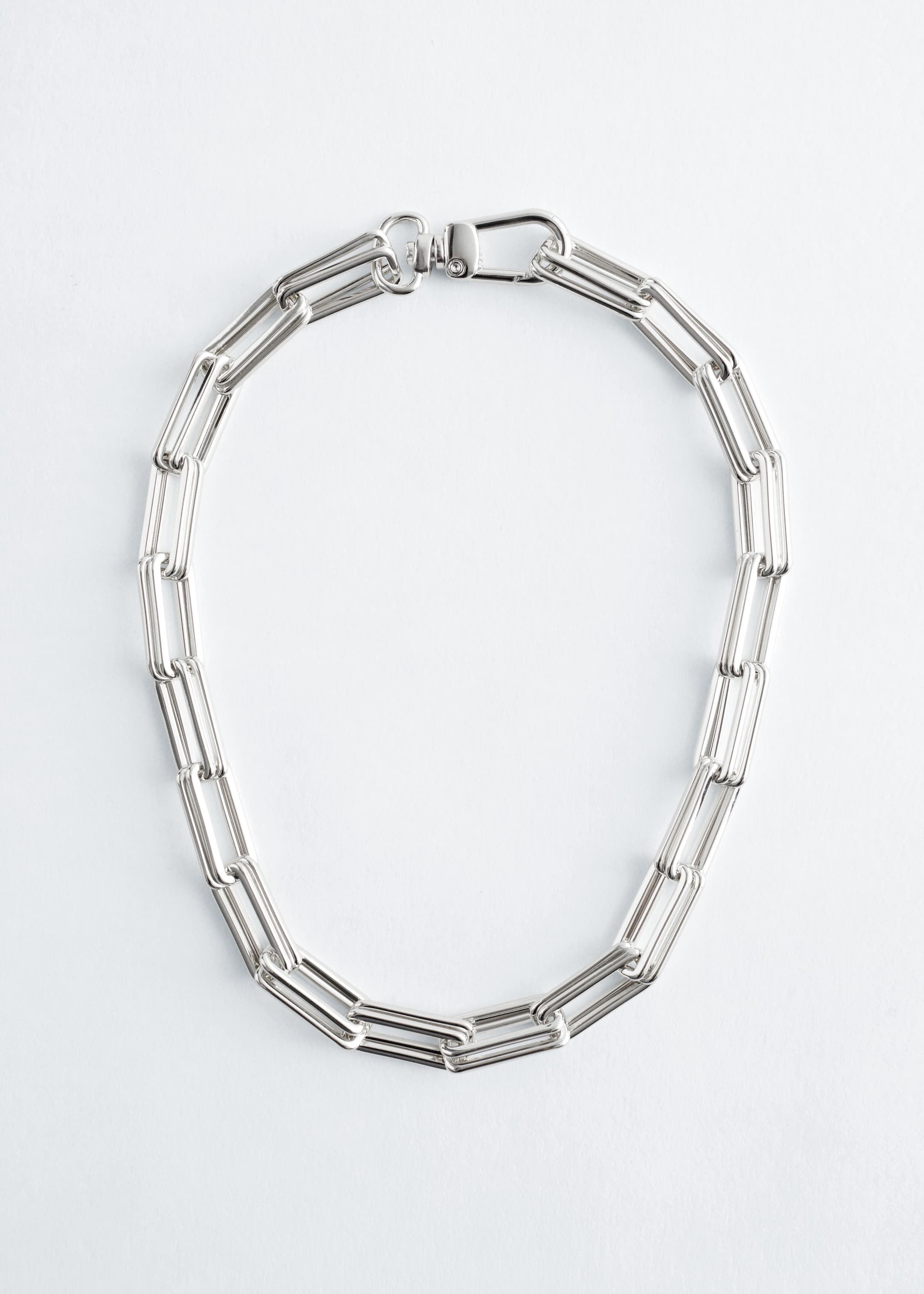 Agrandir l'image: Un collier à maillons épais de couleur argent est posé à plat, formant une forme en U. Il est constitué de maillons rectangulaires allongés et est fermé par un fermoir à mousqueton pivotant, indiquant un ajustement court.