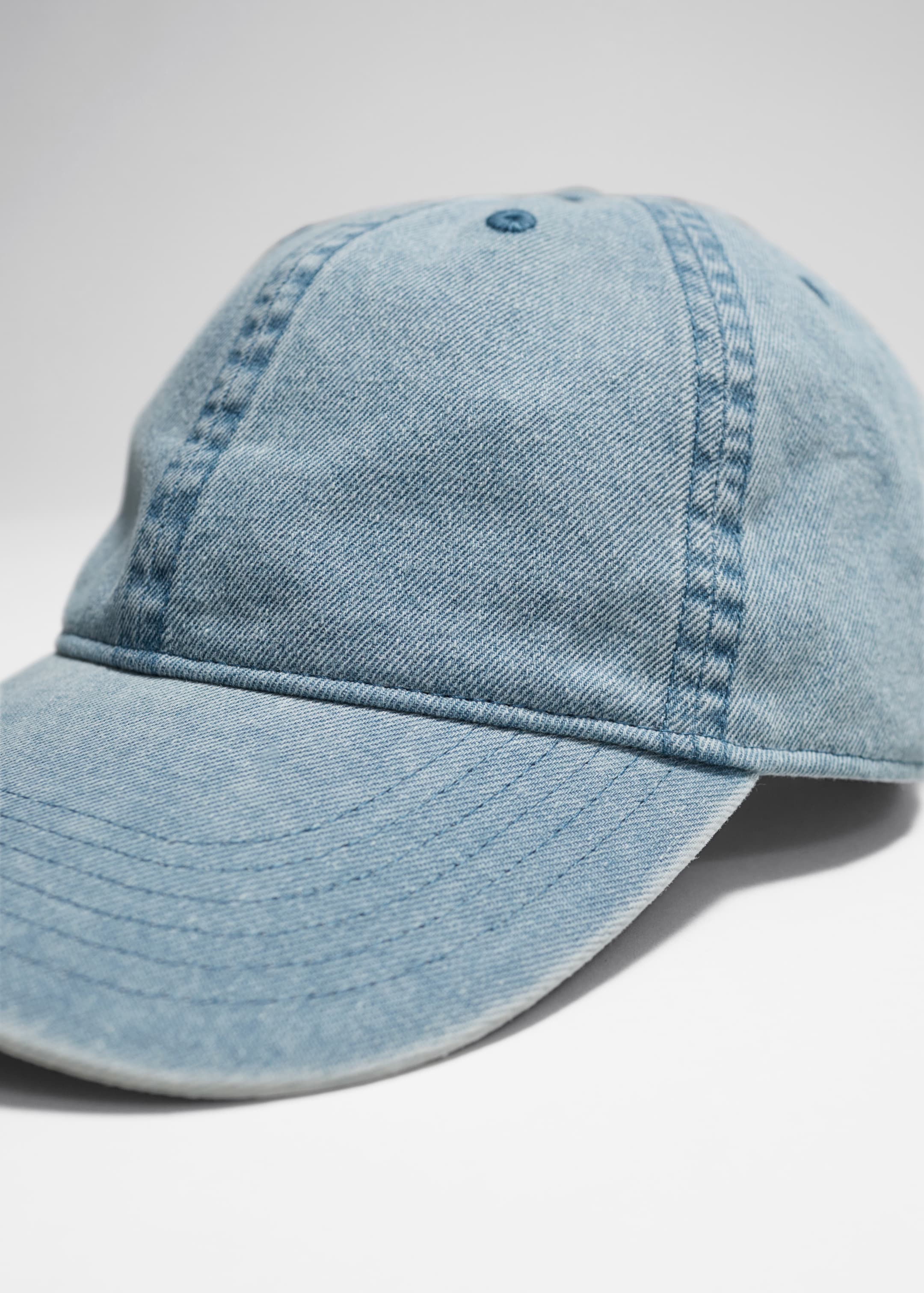 Visualizza immagine più grande: Un berretto da baseball in denim lavato azzurro è presentato in angolazione, mettendo in mostra la sua corona a sei pannelli con cuciture in rilievo e una visiera curva con cuciture parallele. Un piccolo bottone blu è visibile sulla corona.