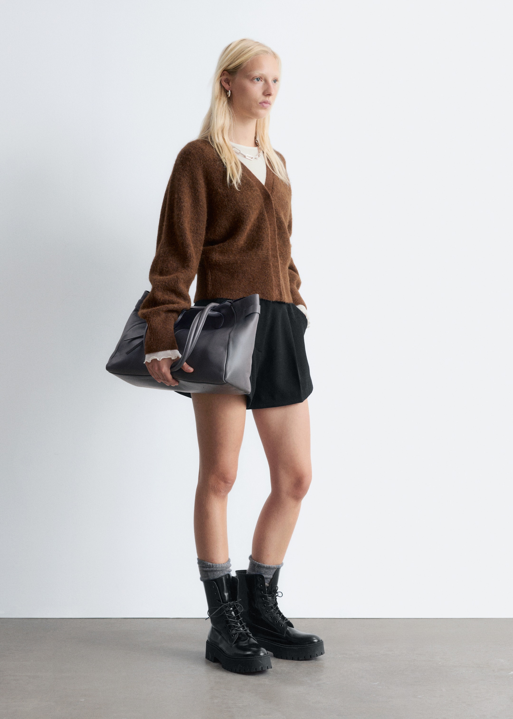 Ingrandisci l'immagine: Un cardigan in maglia spazzolata marrone viene presentato da un'angolazione frontale a tre quarti. Presenta uno scollo a V, maniche lunghe e una vestibilità rilassata e corta, indossato aperto sopra un top bianco.