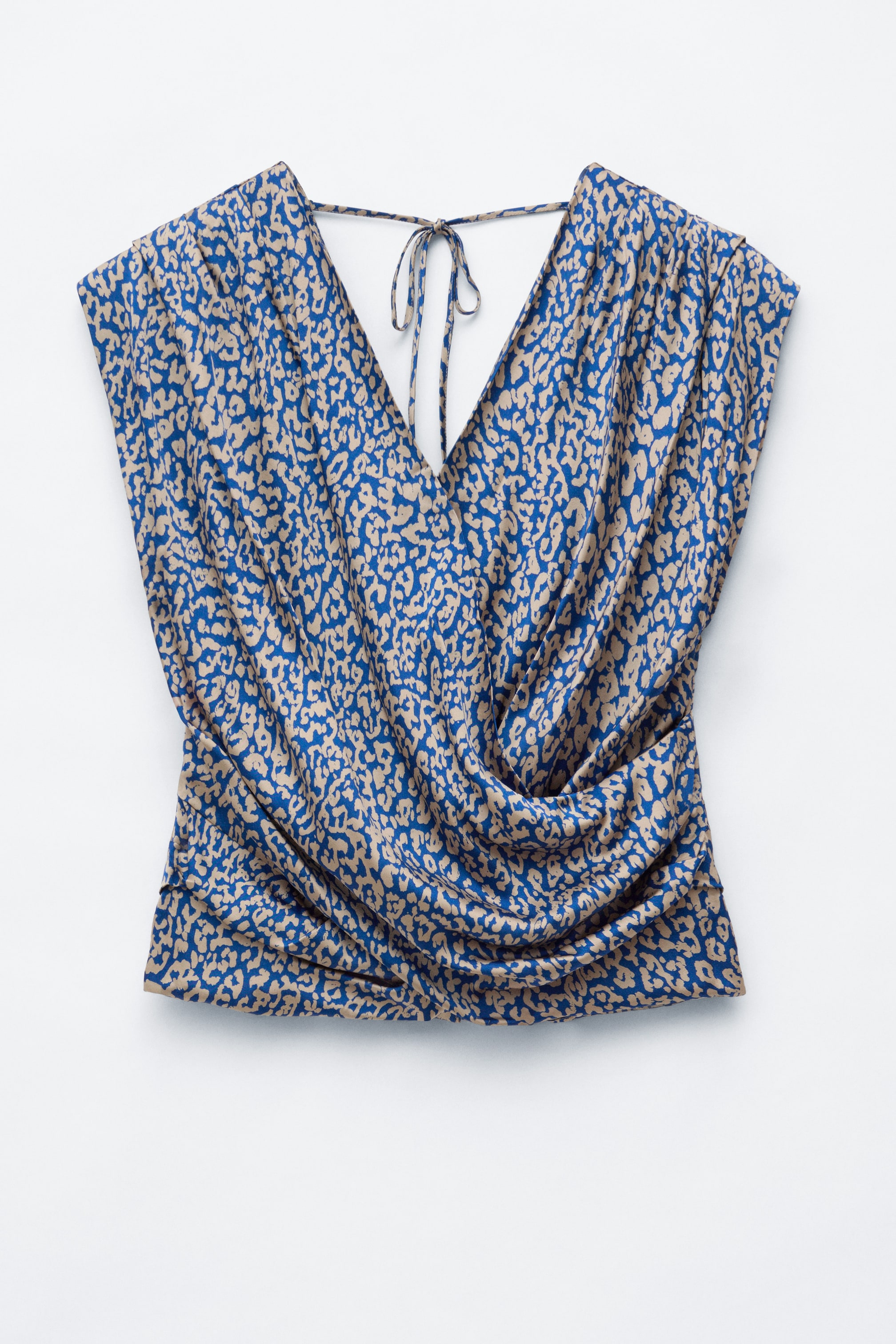 View larger image: A sleeveless wrap top shown from the front features a blue and beige animal print, a draped V-neckline, and pleated details at the shoulders and sides. The top gathers into a ruched front, with a thin fabric tie visible at the back of the neck.