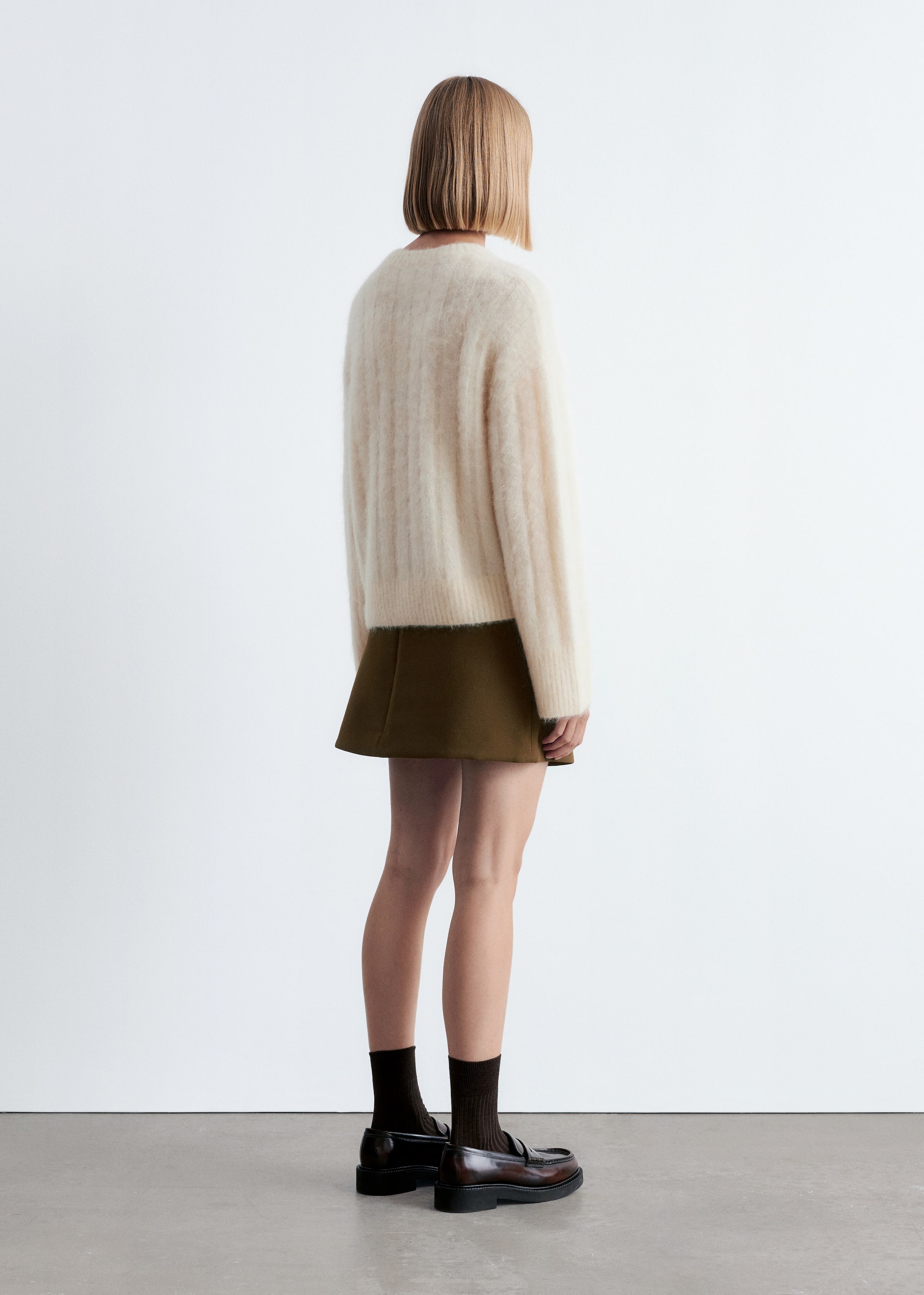 View larger image: A cream-colored, fuzzy ribbed knit sweater is being displayed from the back and partial side view, featuring long, relaxed sleeves and a straight hemline. It is being paired with an olive green A-line mini skirt, dark brown ribbed socks, and chunky brown loafers.