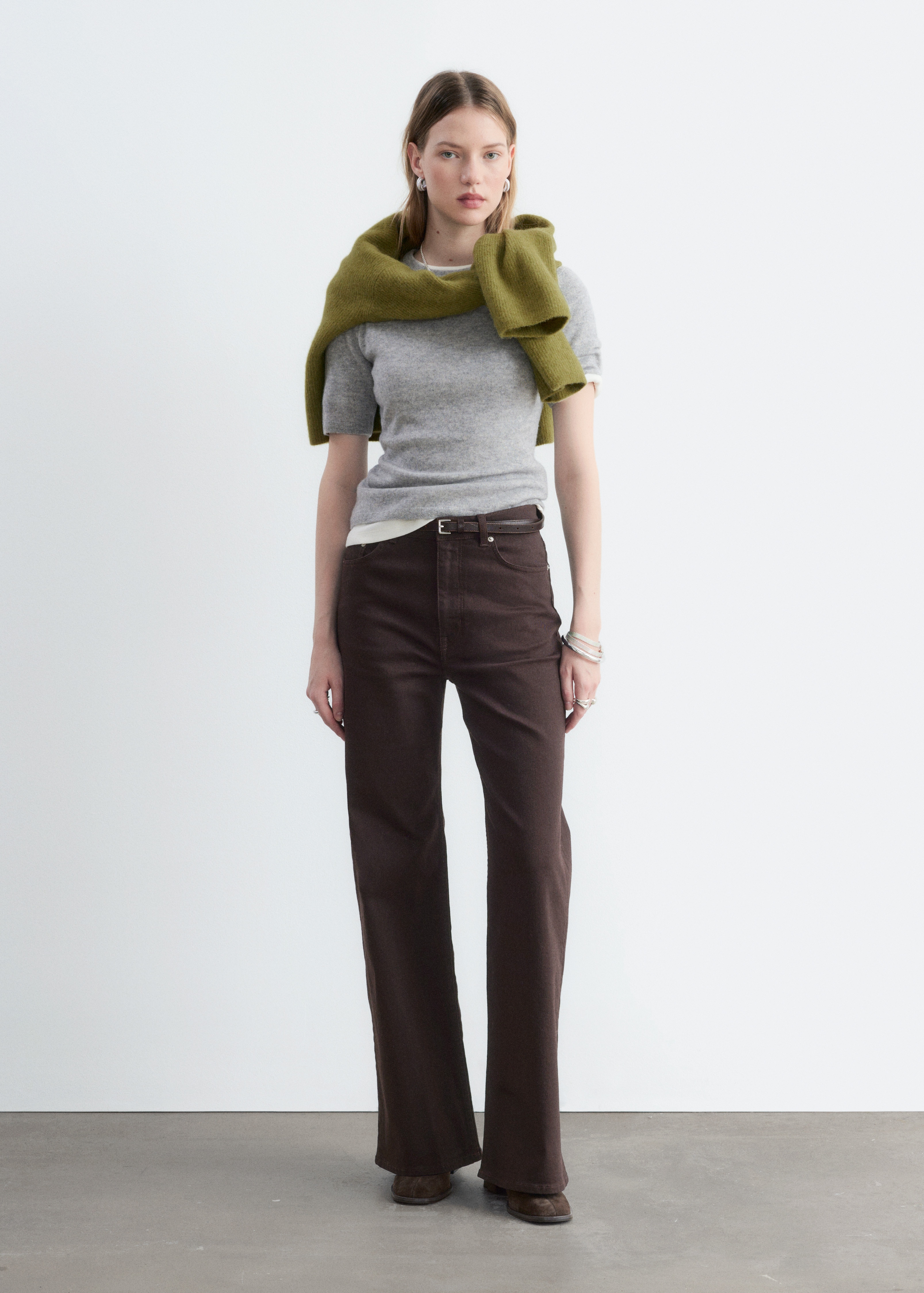 Ett par mörkbruna, högmidjade, vida jeans presenteras framifrån, med en klassisk femficksdesign i denim som har synliga framfickor, metallnitar och en knapp- och dragkedjestängning.
