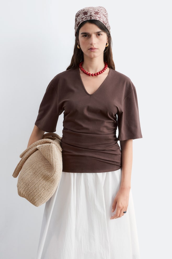 A brown V-neck top featuring three-quarter dolman sleeves. It showcases gathering details along the sides, creating a fitted silhouette. - 1