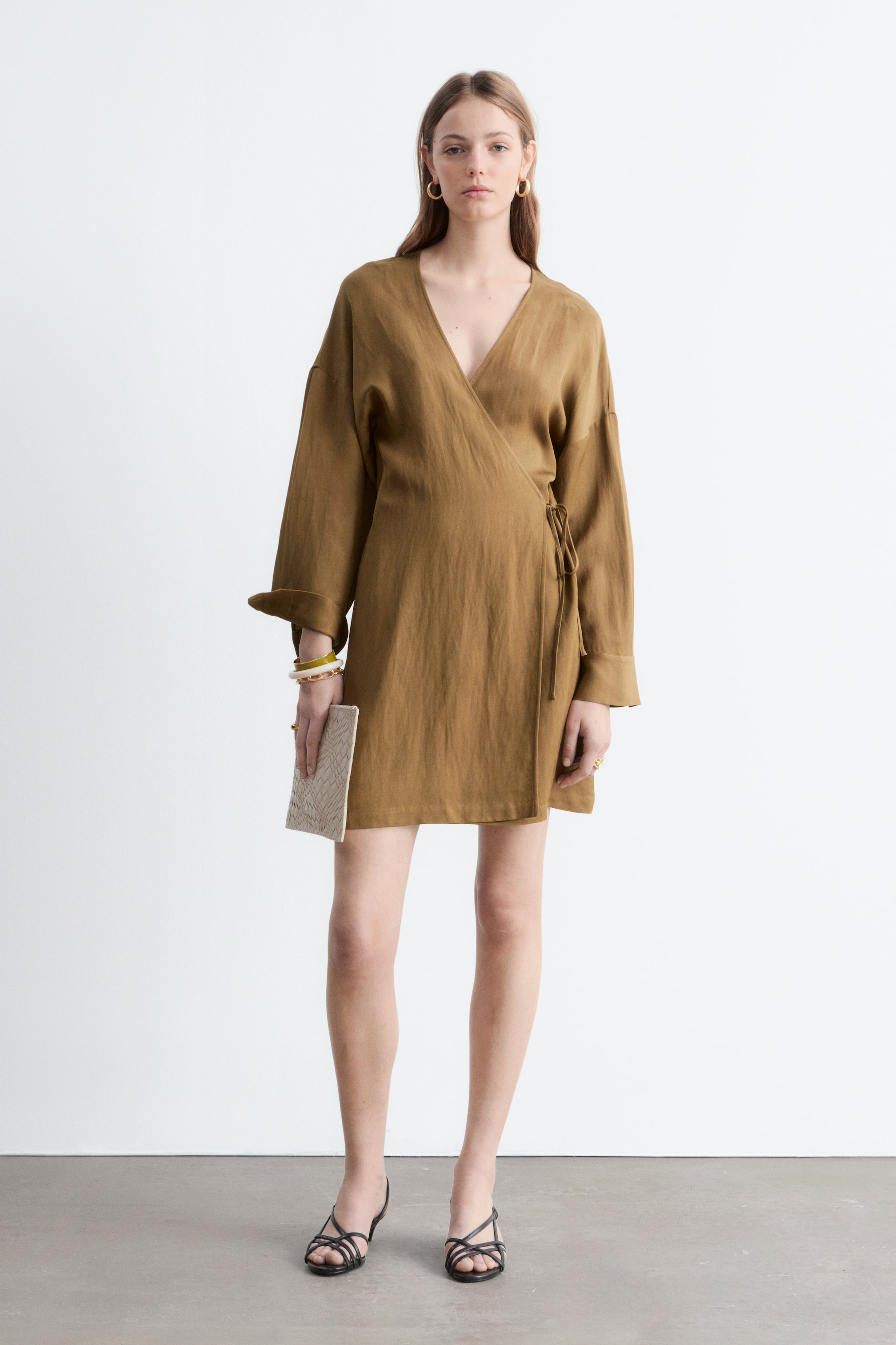 Se større billede: En olivenbrun slå-om kjole præsenterer en V-udskæring og lange ærmer med opsmøgede manchetter, med sidebindebånd og en længde over knæet.
