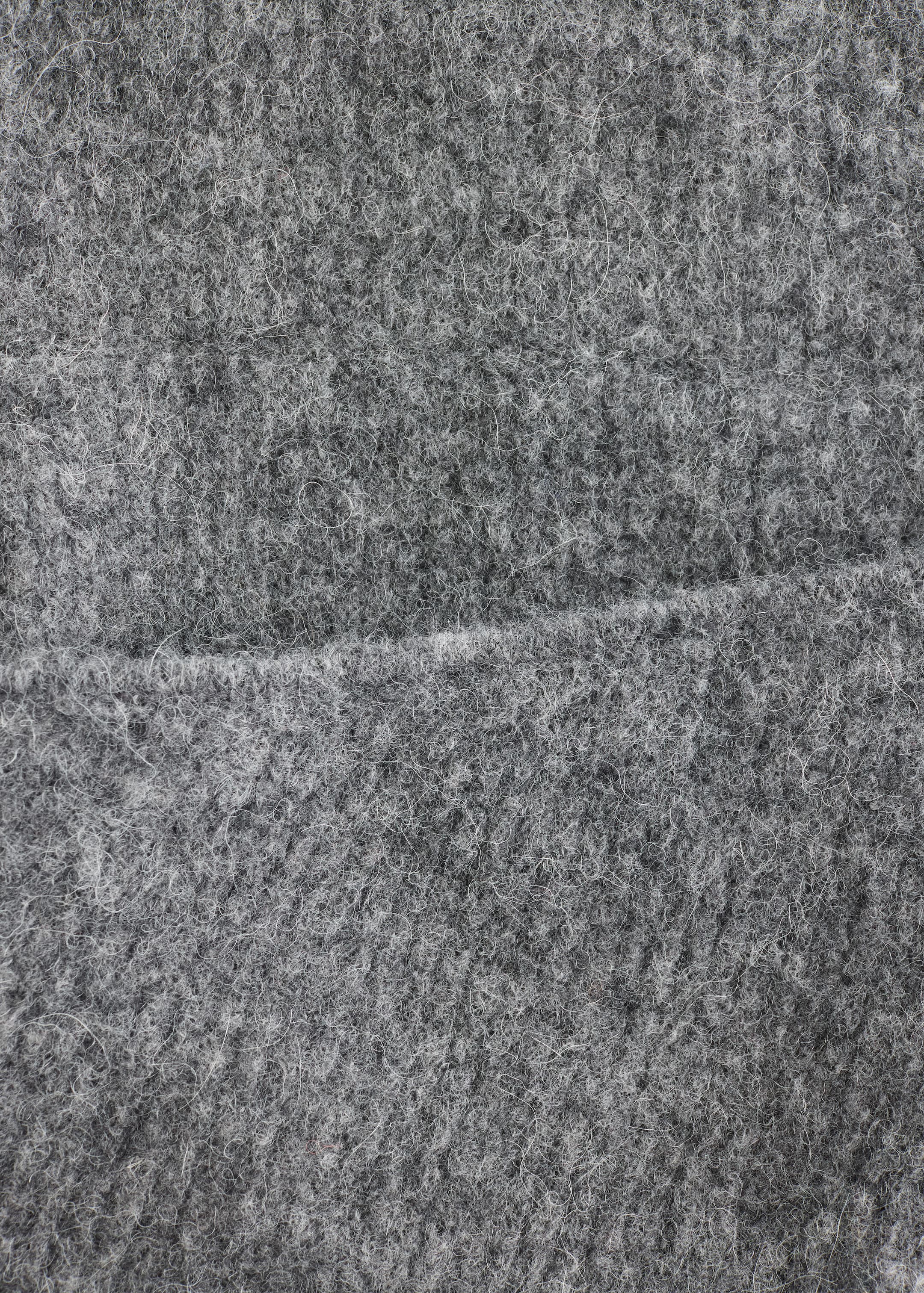 Größeres Bild ansehen: Ein grauer Stoff zeigt eine dichte, flauschige Textur mit sichtbaren hellgrauen Fasern, und eine horizontale Naht verläuft quer über seine Mitte.