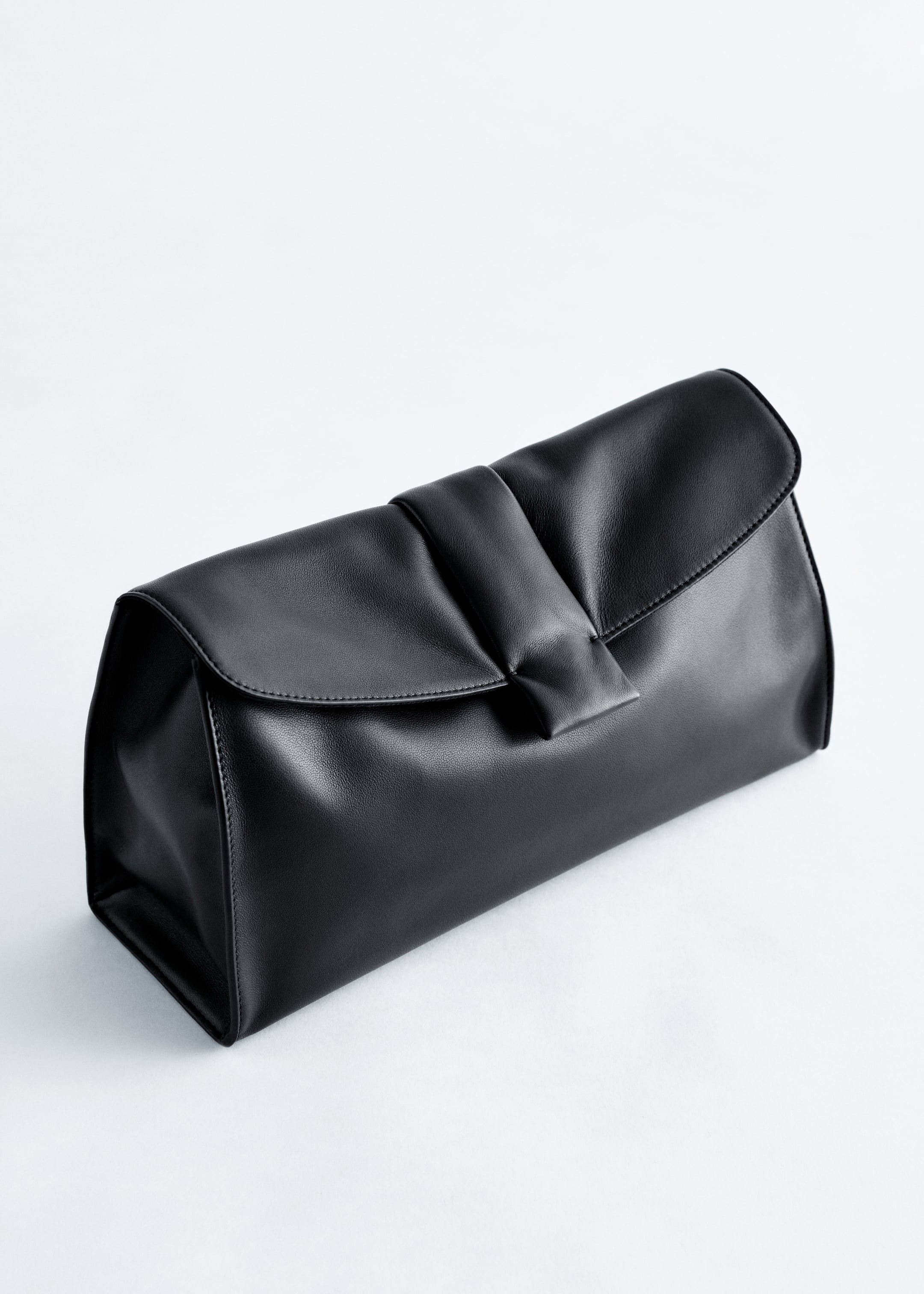 Größeres Bild ansehen: Eine schwarze Lederclutch ist nach VORNE ausgerichtet und leicht angewinkelt positioniert. Sie verfügt über einen weichen, rechteckigen Körper und einen Klappverschluss mit einer zentralen, gerafften Falte.