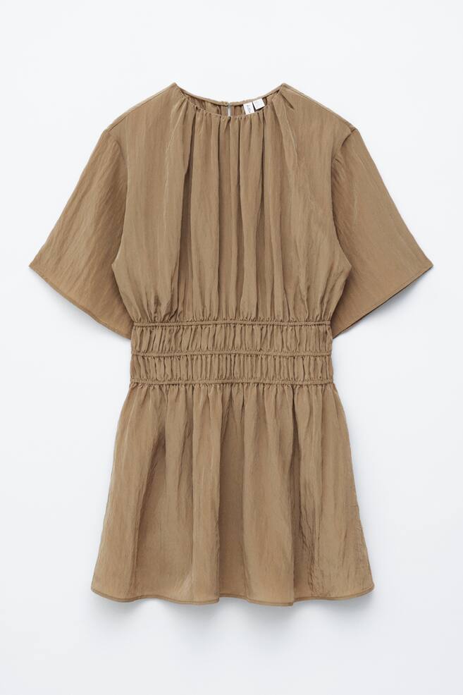 The light brown dress is displayed FRONT, featuring a gathered round neckline and short sleeves. It showcases an elasticated shirred waistline, which flows into a gathered skirt with a subtle crinkled texture. - 1