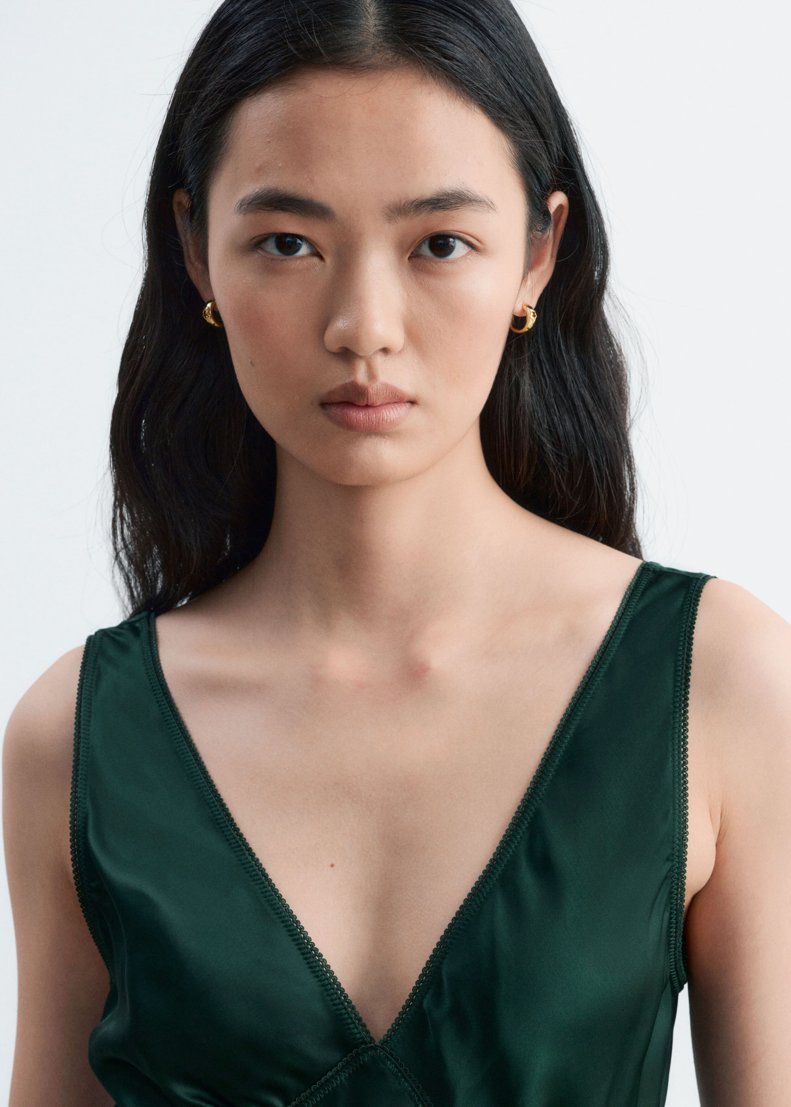 A dark green satin slip dress with a deep V-neckline and delicate lace trim is being worn by the model.