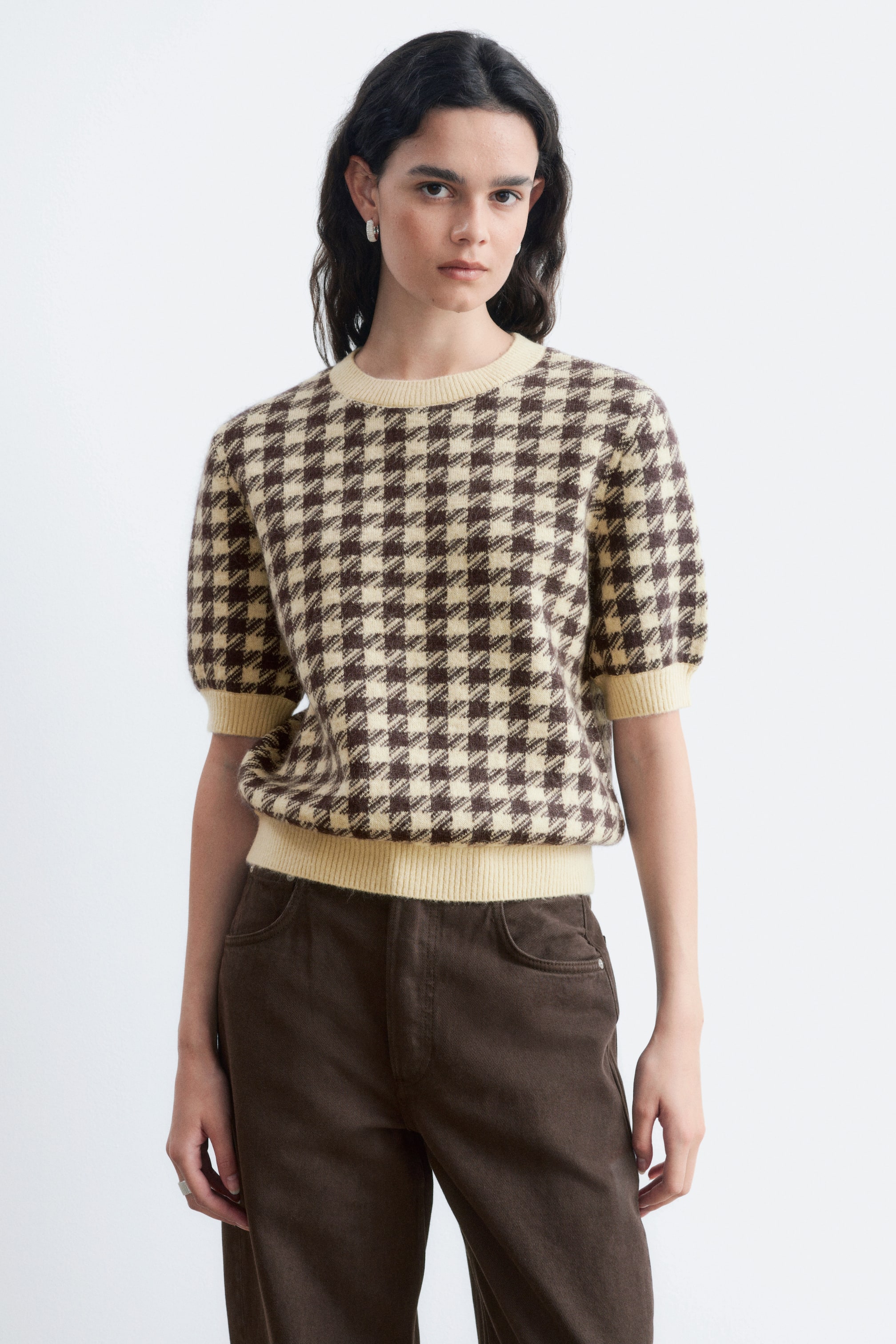 Visualizza immagine più grande: La modella indossa un top a maniche corte in maglia con motivo jacquard crema e marrone. Presenta girocollo, maniche corte a sbuffo e bordi a coste su collo, polsini e orlo.