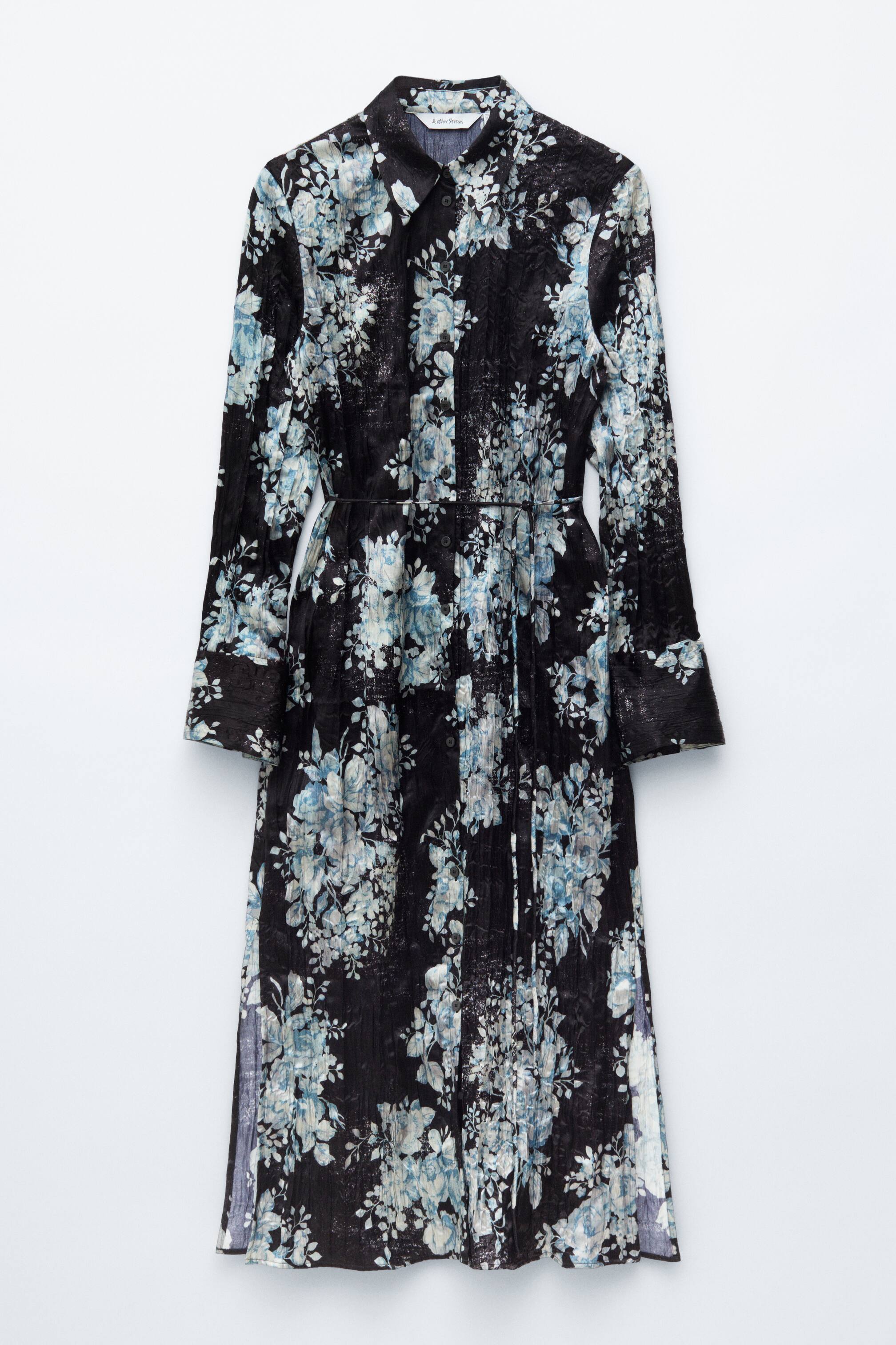 Vezi imaginea mai mare: O rochie cămașă midi neagră afișează un imprimeu floral distressed în albastru deschis și alb, prezentând o vedere frontală. Aceasta are un guler ascuțit, o plachetă completă cu nasturi în față și mâneci lungi cu manșete cu nasturi. Rochia este strânsă în talie cu un cordon subțire și se transformă într-o fustă plisată vertical.