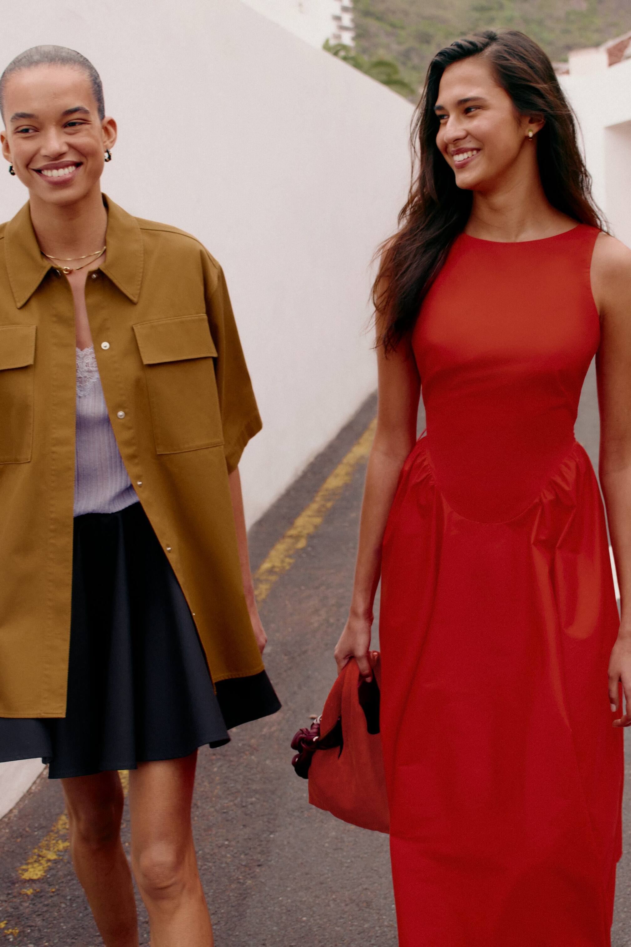 Nagyobb kép megtekintése: Egy piros ujjatlan ruha látható elölről-jobbról, amely magas, kerek nyakkivágással, testhezálló felsőrésszel és teljes, ráncolt szoknyával rendelkezik, amely bokáig ér a karcsúsított derékvonaltól. Egy hozzáillő piros táska van mellette tartva.