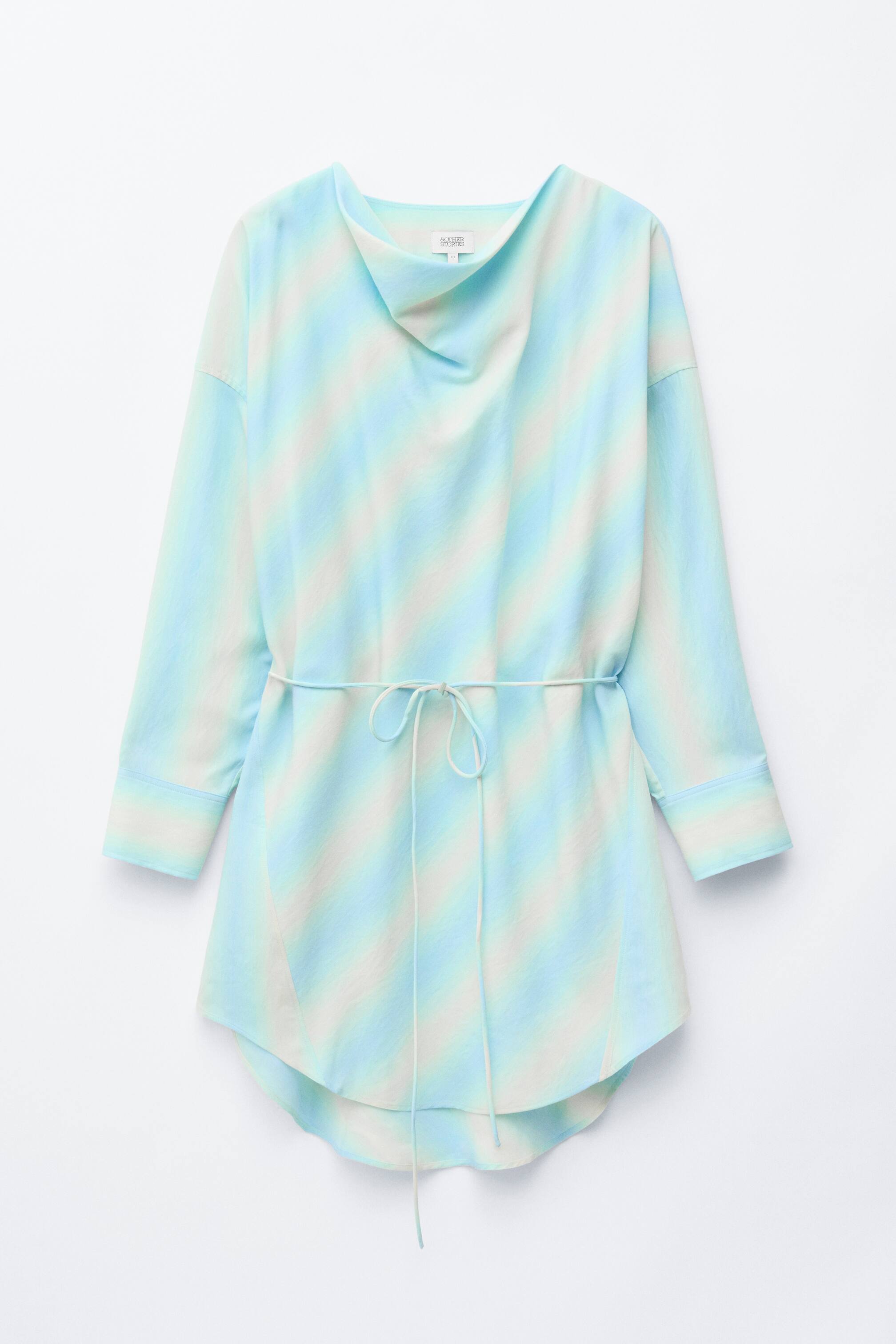 Näytä suurempi kuva: Edestäpäin katsottuna tunika esittelee vinoraitoja vaaleansinisen, mintunvihreän ja valkoisen sävyissä, luoden liukuväriefektin. Siinä on drapeerattu kaulus, pitkät hihat nappimanseteilla, ohut valkoinen solmittava vyönauha, joka solmitaan eteen ja kiristää vyötäröä, sekä kaareva high-low helma.