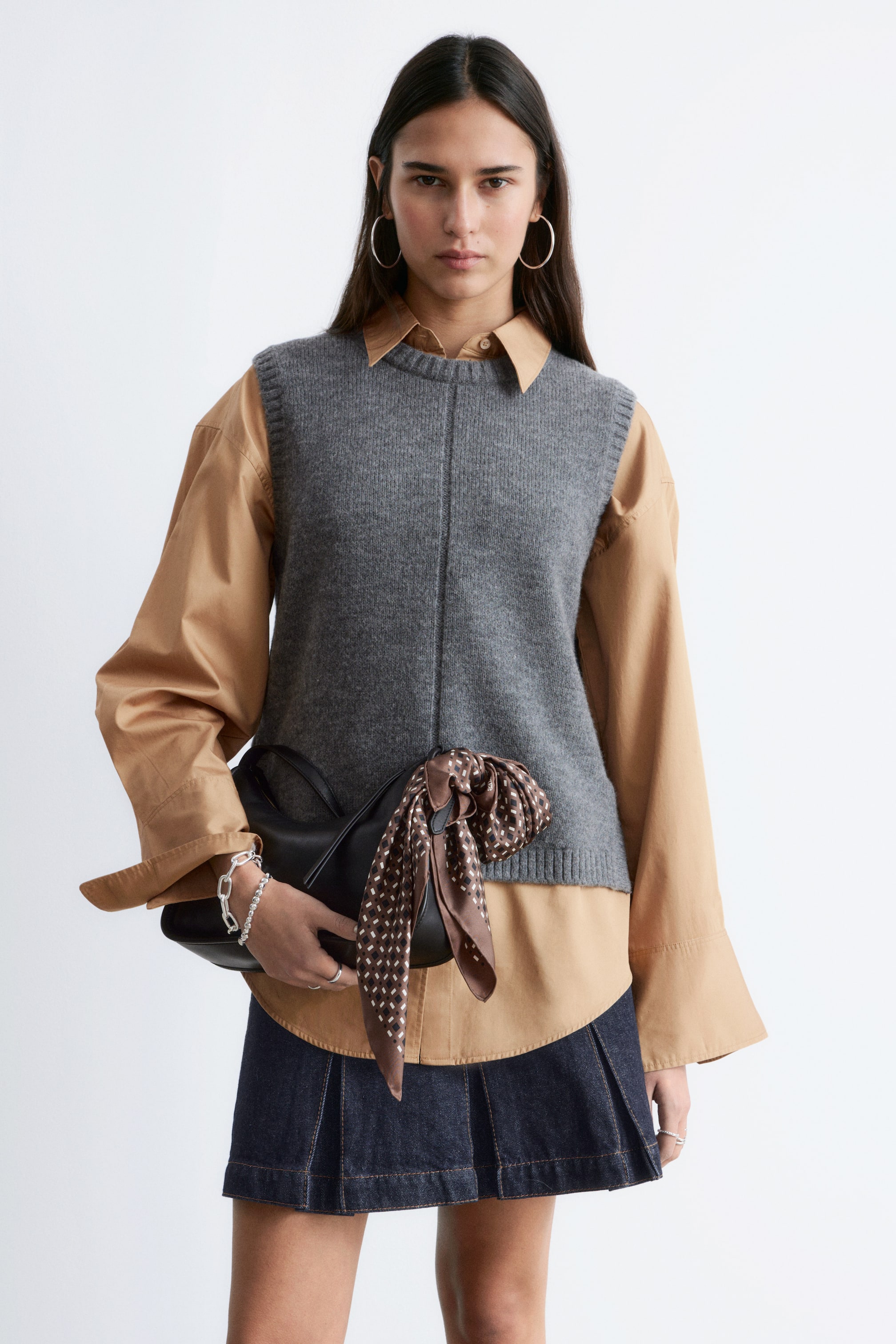 View larger image: A grey sweater vest is worn over a tan collared shirt, featuring a round neckline, ribbed armholes and hem, and a vertical knit detail down the front.