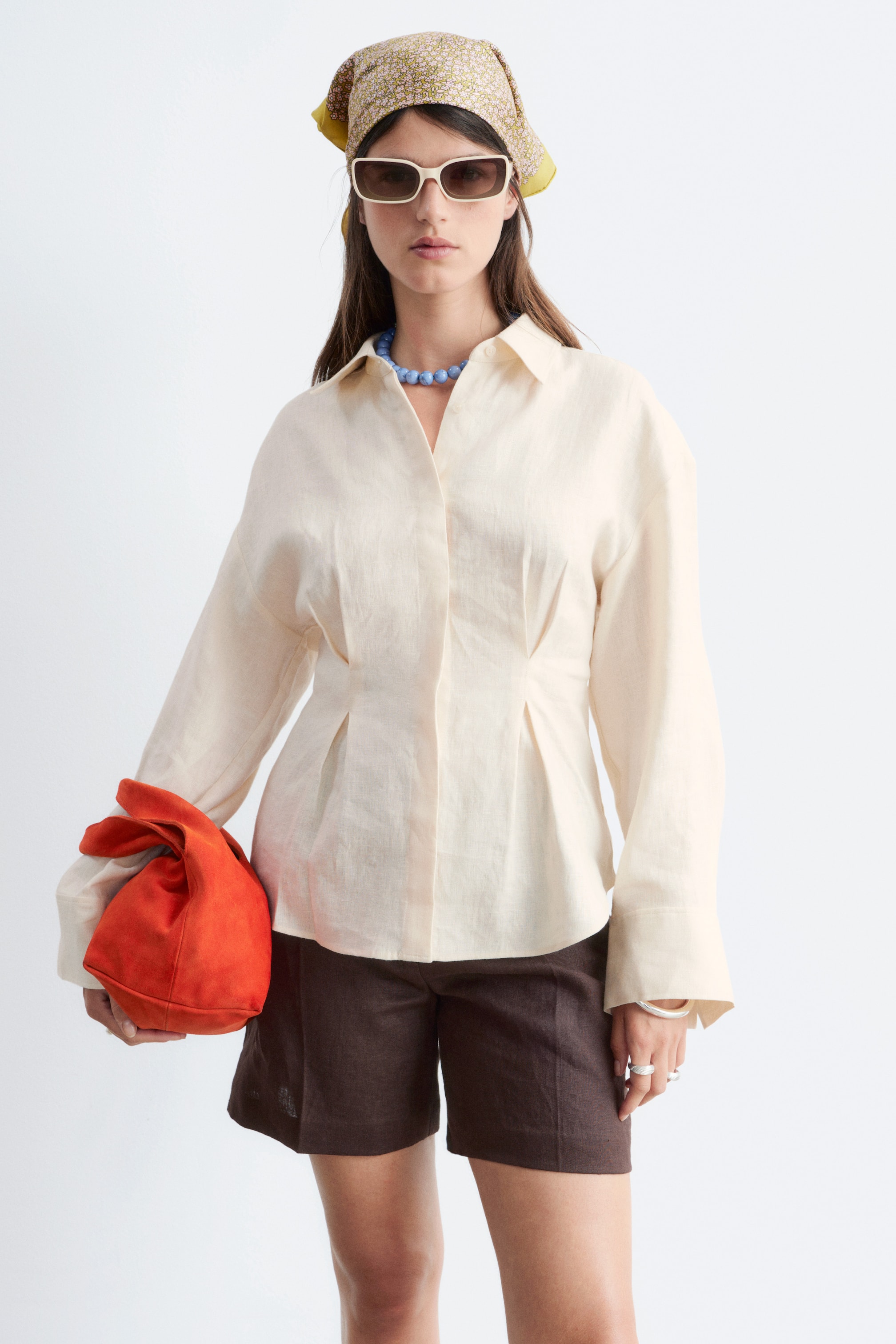 Visa större bild: En ljusbeige linneskjorta med spetsig krage och långa ärmar med breda manschetter. Den är designad med vertikala veck framtill, vilket skapar en figursydd midja.