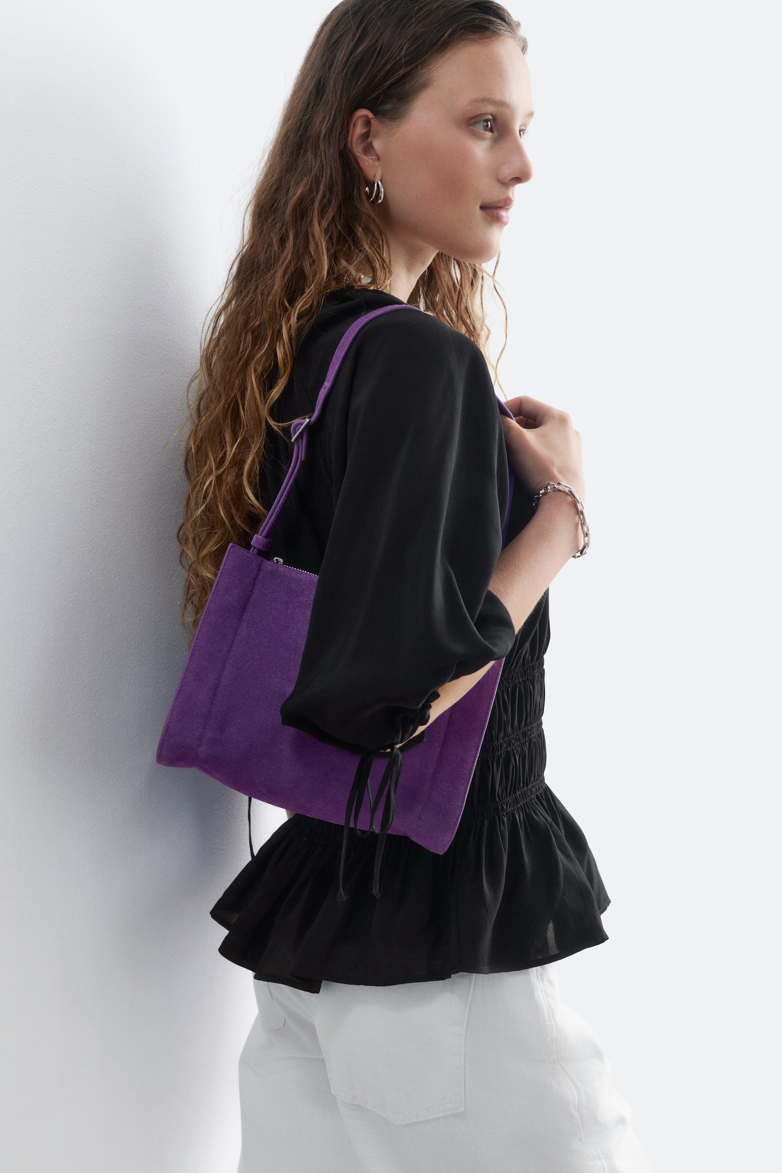 Un sac bandoulière rectangulaire en daim violet avec une séparation, vu de face, doté d'une fermeture éclair sur le dessus et d'une fine sangle réglable s'étendant vers le haut. - 1