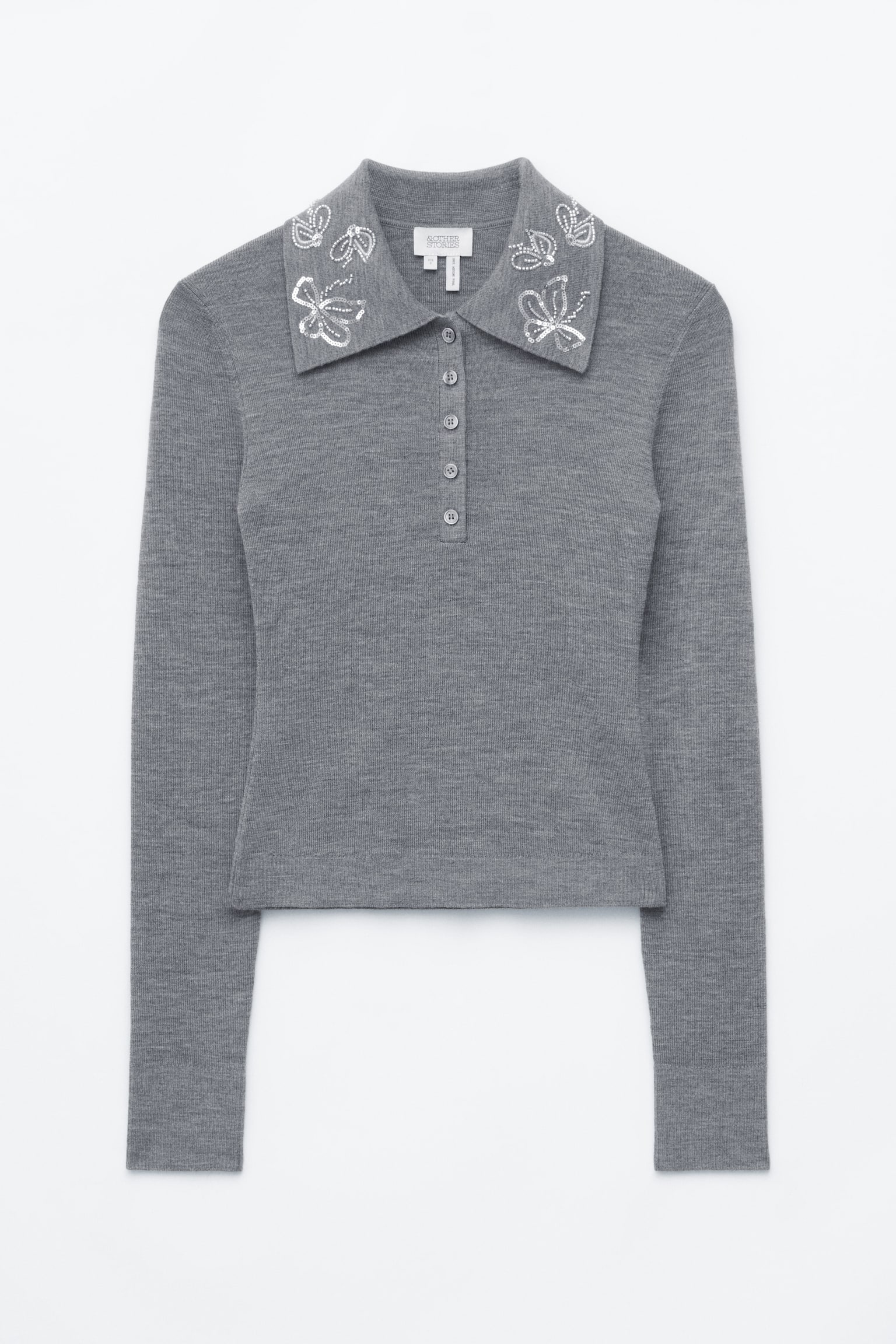 Un maglione polo in lana grigia mostra una vestibilitÃ  slim-fit sul davanti, mettendo in risalto un colletto a punta impreziosito da un ricamo a farfalla con paillettes argentate. Il maglione presenta una chiusura a cinque bottoni sul petto e maniche lunghe con polsini a coste.