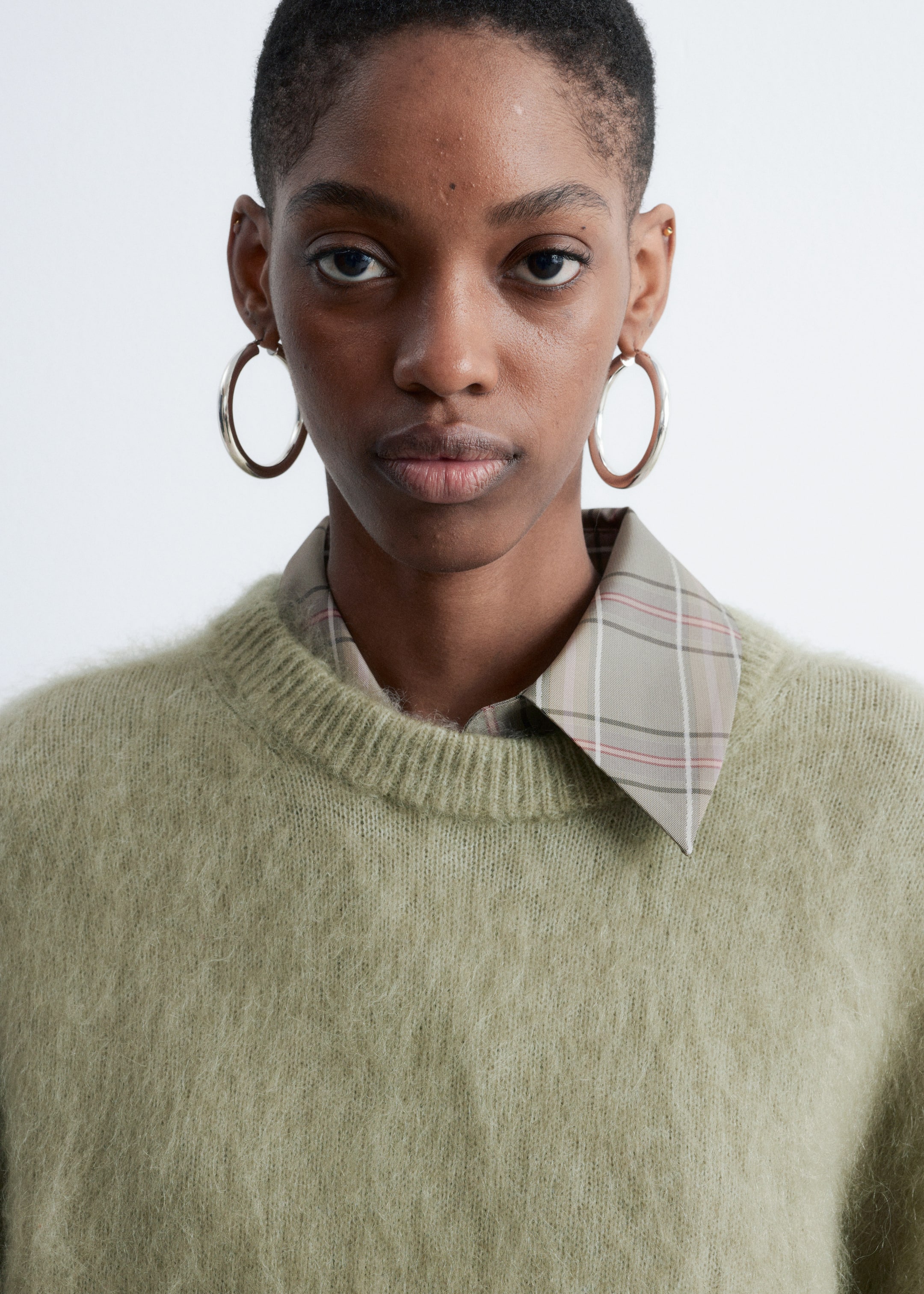 Visa större bild: En ljusgrön, fluffig stickad crewneck-tröja bärs, med en ribbad halsringning. En beige rutig skjorta med krage läggs under, med kragens spetsar som sträcker sig över tröjans halsringning.