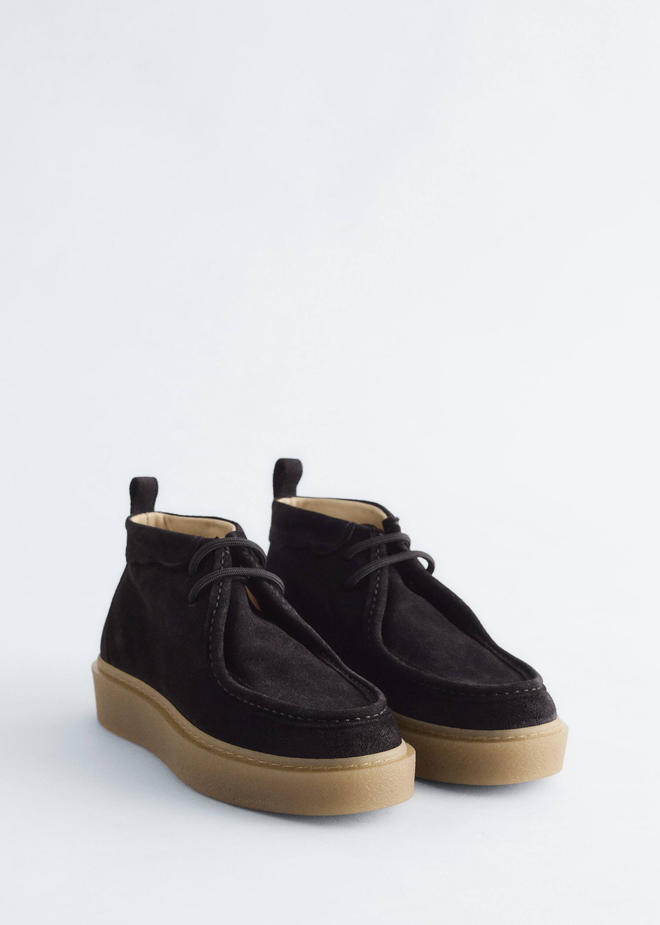 Agrandir l'image: Une paire de bottines en daim foncé est présentée, avec des lacets ronds et un bord festonné brut autour de l'ouverture. Chaque botte est dotée d'une languette à l'arrière et repose sur une semelle plateforme beige avec une surface légèrement texturée.