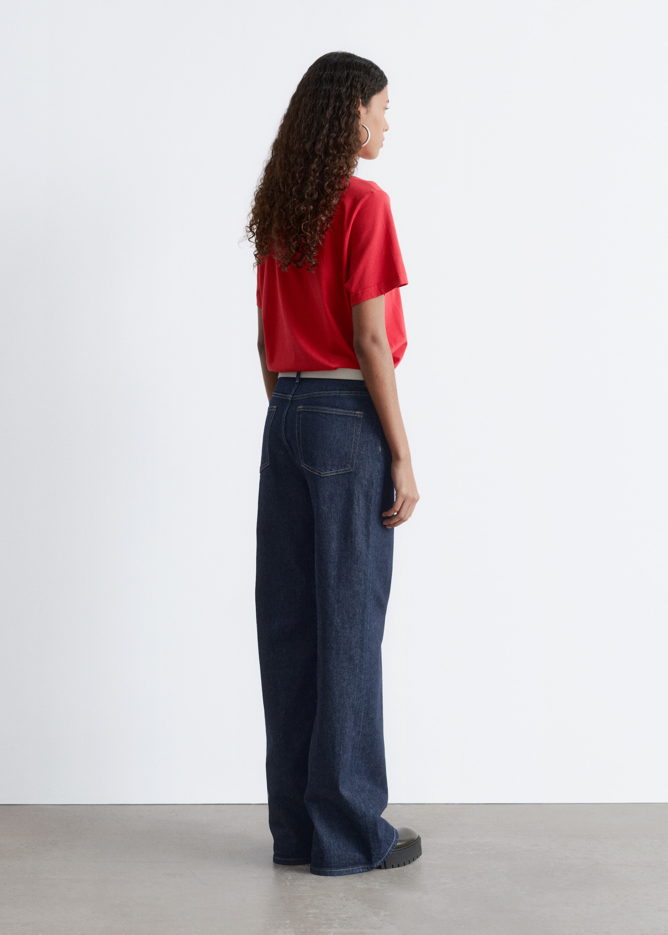 View larger image: A red short-sleeve crewneck t-shirt with a relaxed silhouette is being worn by the model. The t-shirt is partially tucked into dark wash jeans, revealing a light-colored belt.