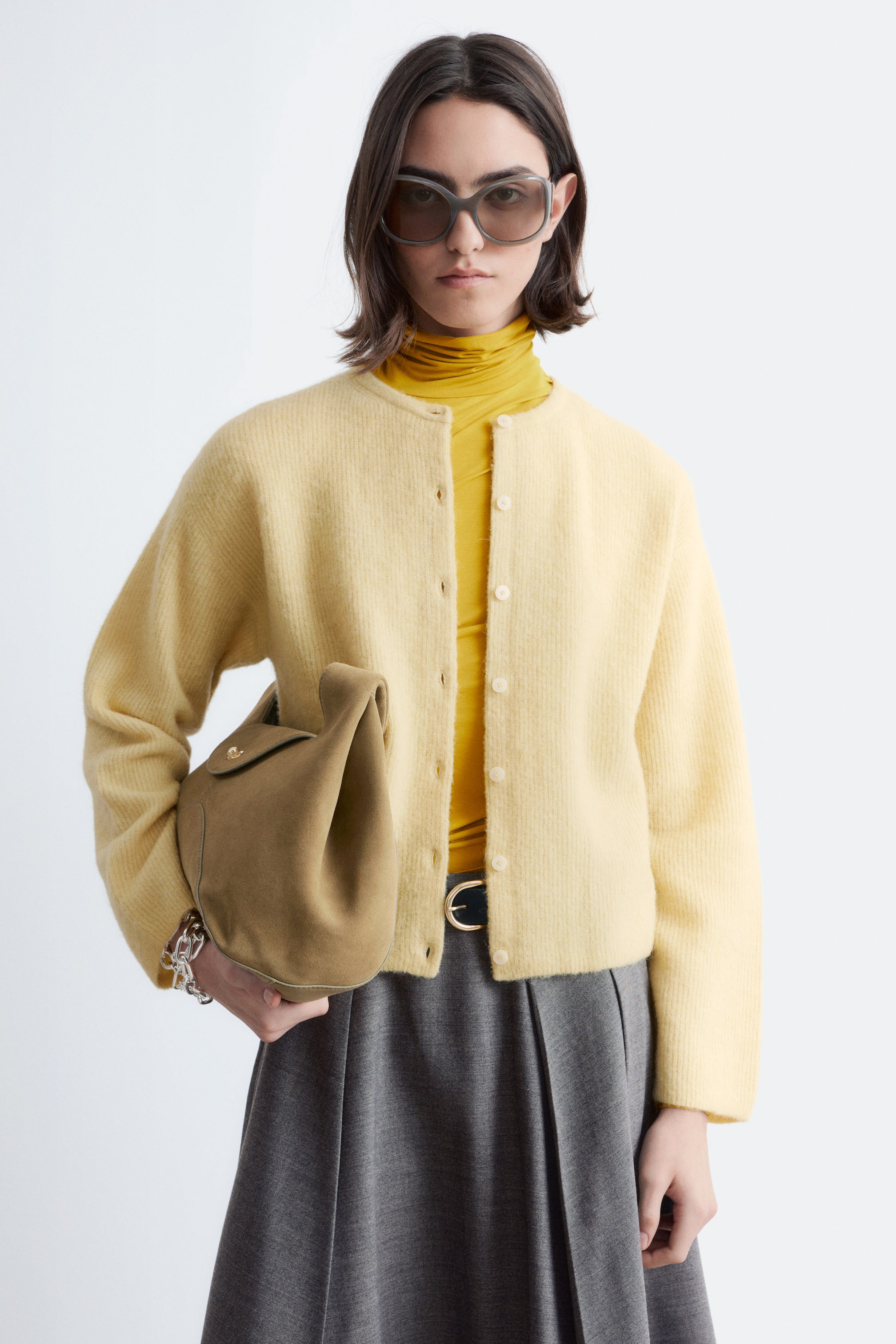 Προβολή μεγαλύτερης εικόνας: Ένα ανοιχτό κίτρινο χνουδωτό ζακέτα παρουσιάζεται με την πρόσοψη, διαθέτοντας στρογγυλή λαιμόκοψη και κλείσιμο με κουμπιά στο μπροστινό μέρος με μικρά, ανοιχτόχρωμα κουμπιά. Φοριέται ανοιχτό, πάνω από ένα κίτρινο ζιβάγκο.