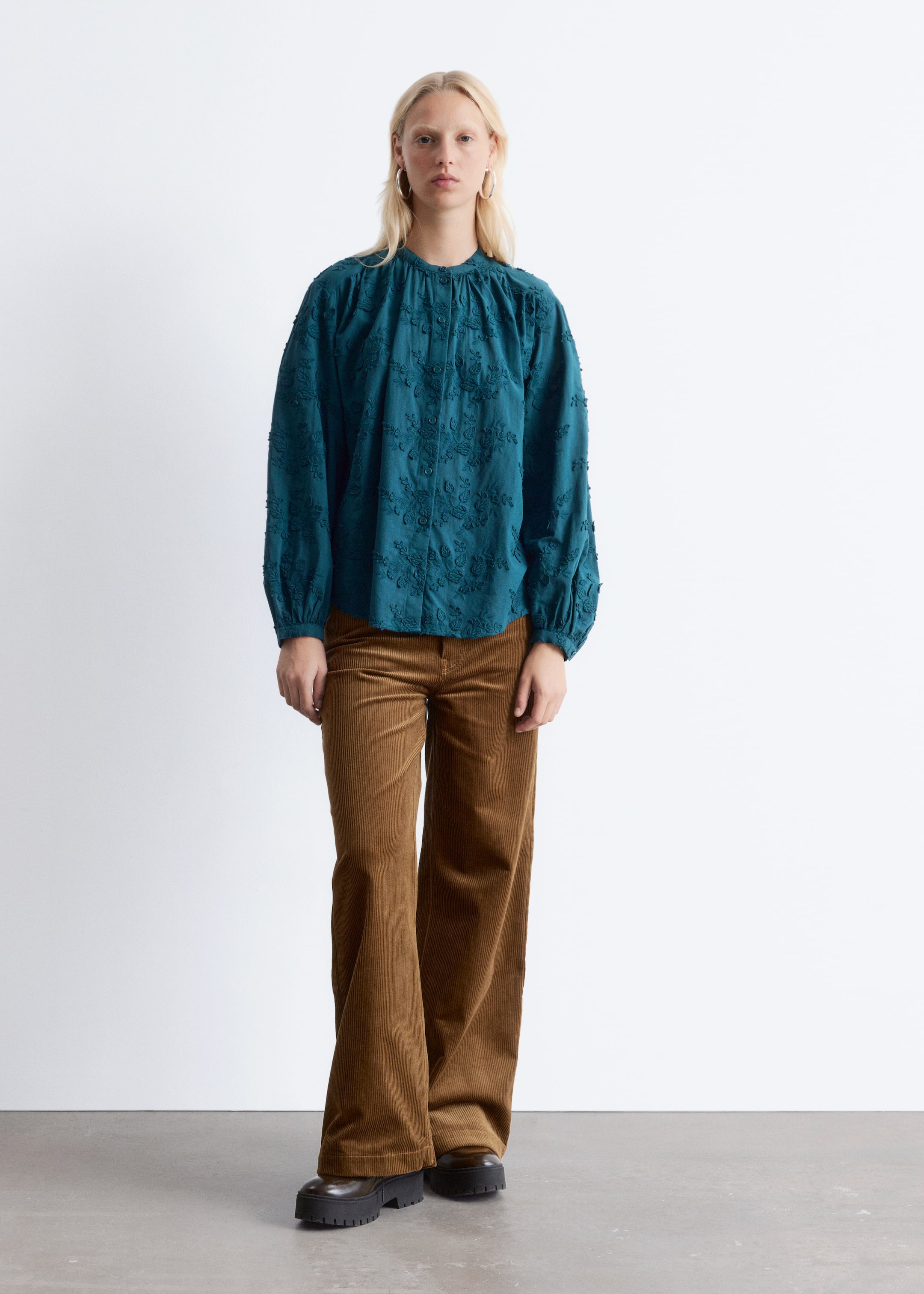 Visualizza immagine più grande: Il prodotto è una blusa verde petrolio con un colletto a fascia arricciato, maniche lunghe e voluminose con polsini elasticizzati e un ricamo floreale strutturato su tutta la superficie, presentando una vestibilità rilassata. È abbinata a pantaloni a gamba larga in velluto a coste marrone, con l'intero ensemble mostrato da un'angolazione frontale diretta.