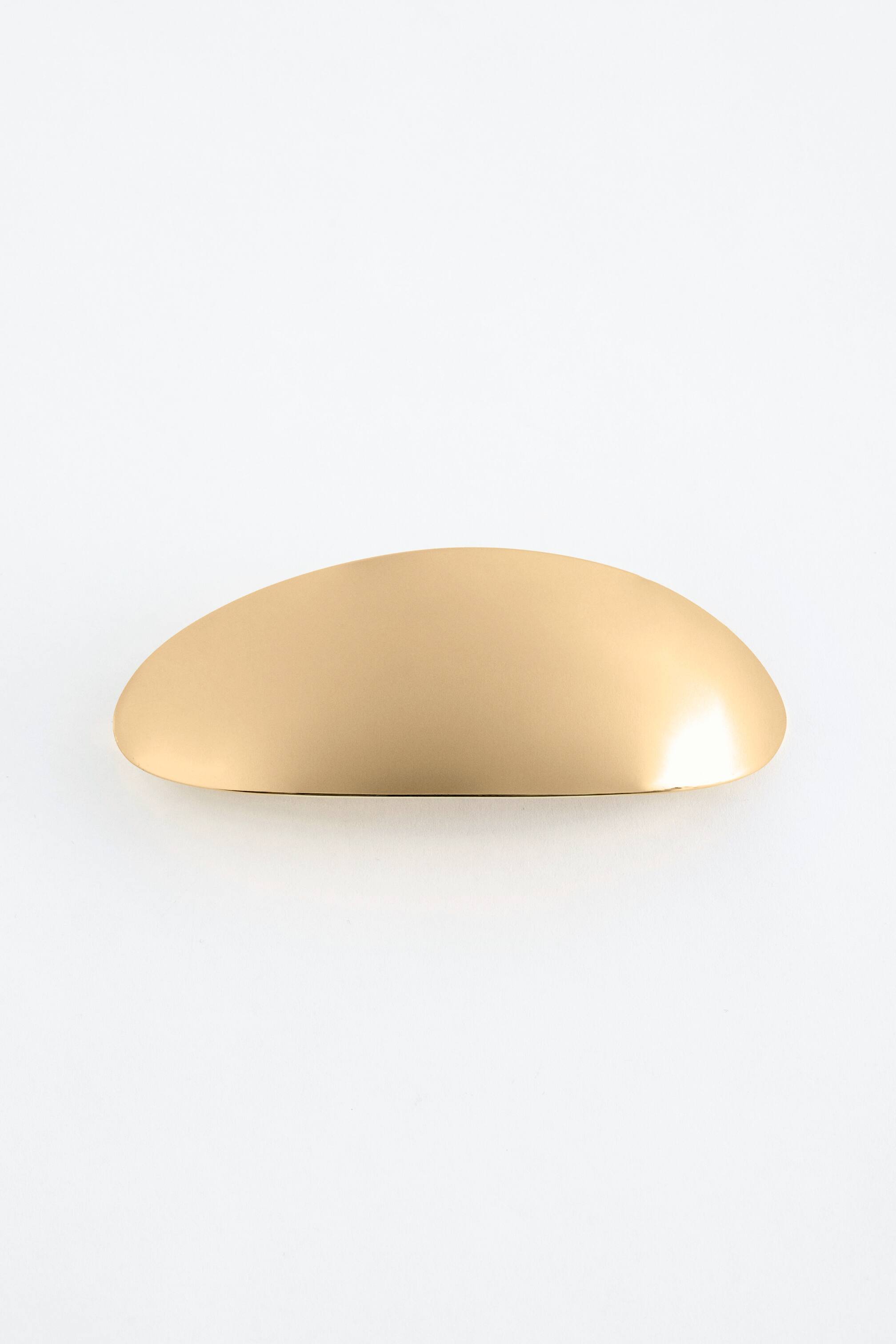 Agrandir l'image: Une barrette dorée est présentée de face, mettant en valeur sa forme élégante, allongée et convexe avec une surface supérieure mate et des bords incurvés subtilement brillants.