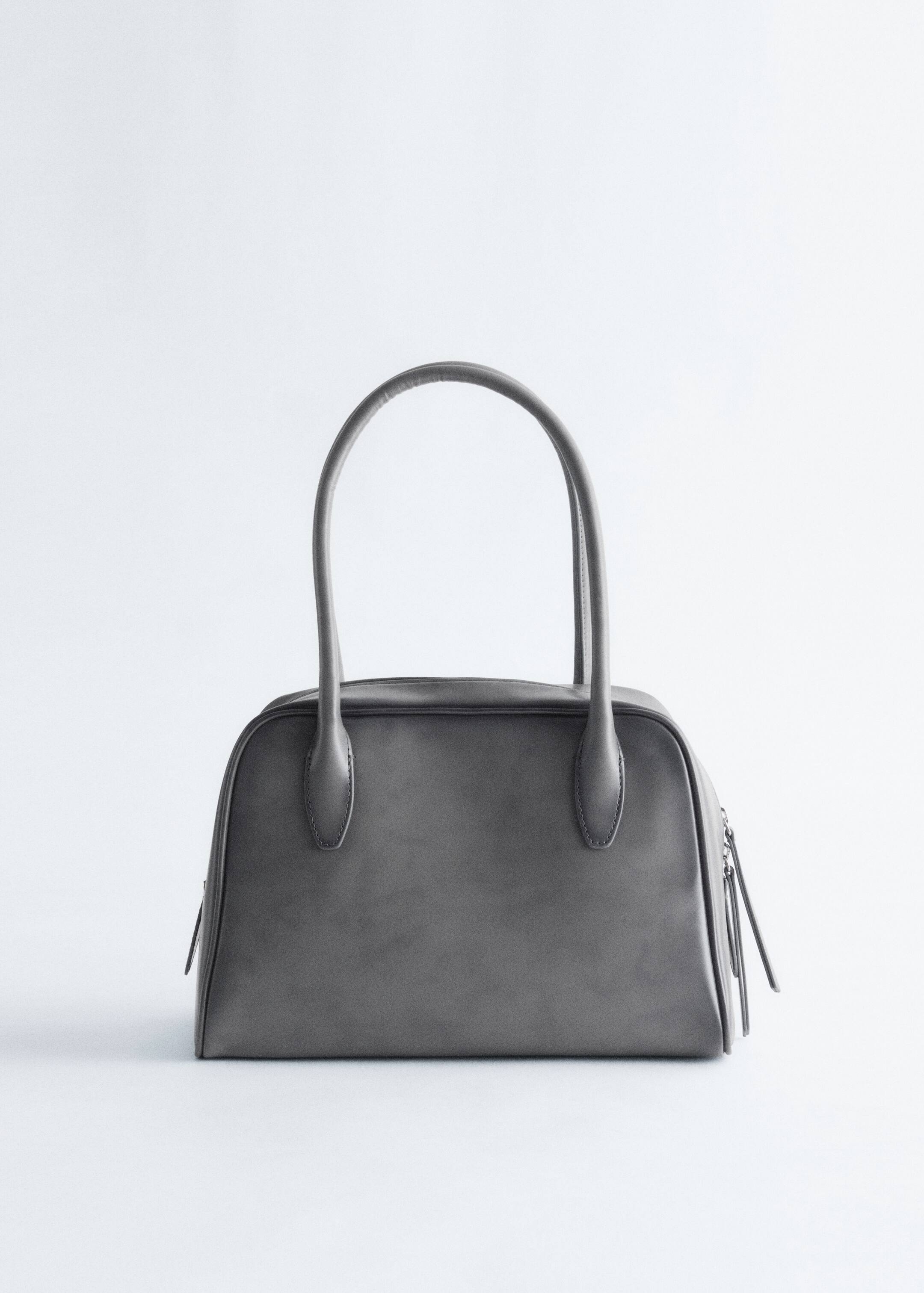 Grösseres Bild ansehen: Eine dunkelgraue Handtasche wird von vorne präsentiert, mit zwei abgerundeten oberen Griffen, die aufrecht stehen. Ein Hauptreißverschluss verläuft entlang der Oberseite, und vertikale Reißverschlüsse mit Zuglaschen sind an beiden Enden der Tasche sichtbar.
