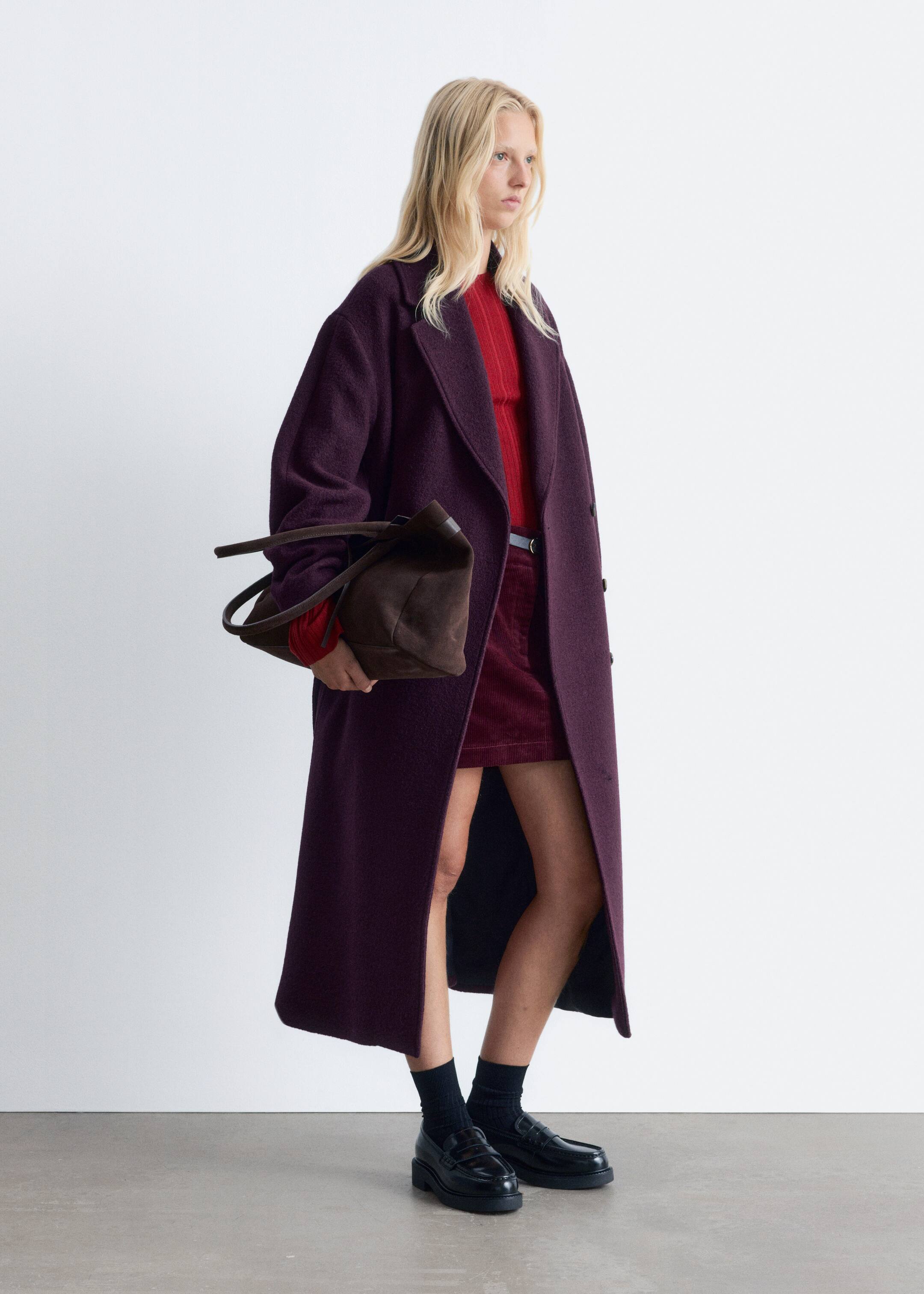 Agrandir l'image: Un long manteau en laine texturée de couleur violet foncé est présenté sous un léger angle latéral, mettant en valeur sa coupe décontractée, ses larges revers crantés et sa fermeture à boutons visible, drapé ouvert pour révéler un style en couches.