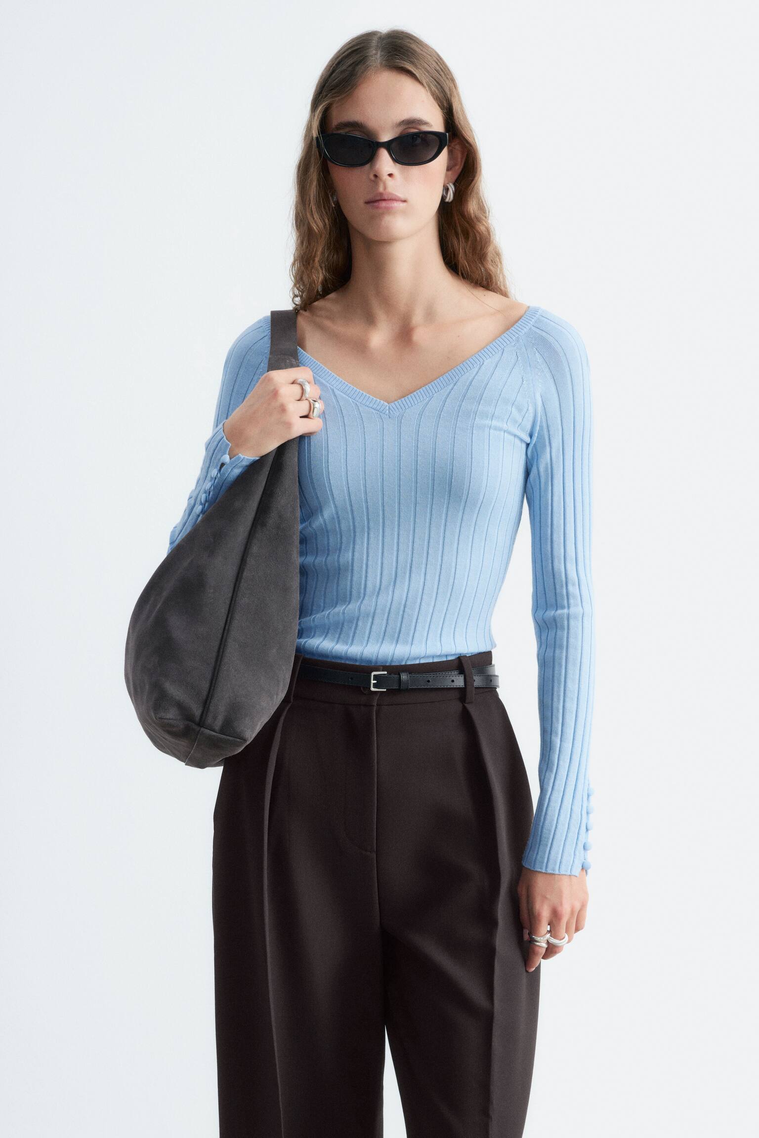Un haut cÃ´telÃ© bleu clair est prÃ©sentÃ© de face, avec un profond dÃ©colletÃ© en V et de longues manches raglan. Sa coupe ajustÃ©e est agrÃ©mentÃ©e d'une rangÃ©e verticale de petits boutons recouverts de tissu, qui ornent les poignets fendus au bas de chaque manche. - 1
