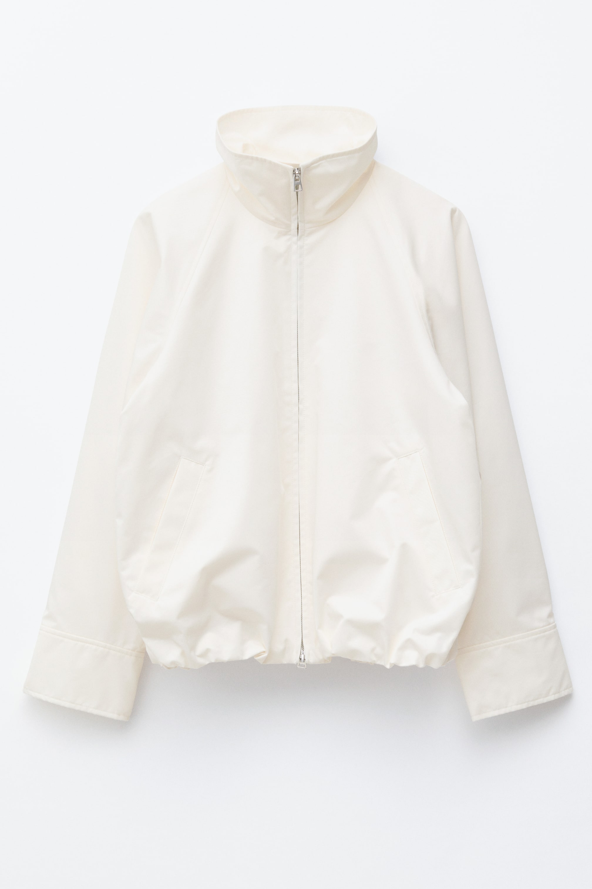 Agrandir l'image: Une veste zippée blanc cassé est présentée de face, dotée d'un col montant, d'une fermeture éclair à double sens à l'avant et de deux poches passepoilées. Son ourlet à cordon de serrage est froncé.