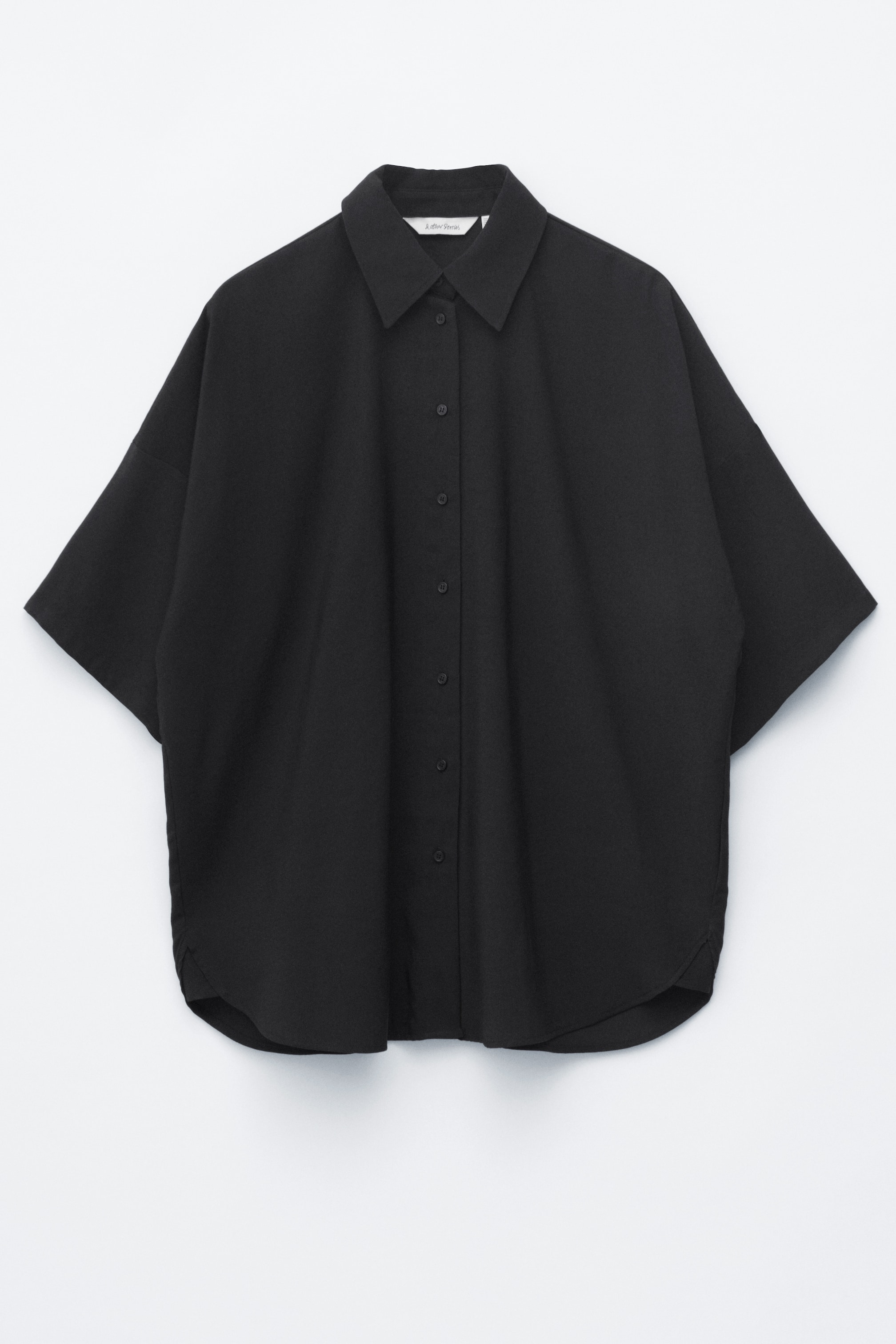 Größeres Bild ansehen: Ein schwarzes, übergroßes Hemd, gewebt aus einem leichten Stoff, wird von vorne präsentiert. Es verfügt über einen klassischen Kragen, einen Knopfverschluss vorne, weite Viertelärmel und einen abgerundeten Saum mit Einsätzen an den Seitennähten.