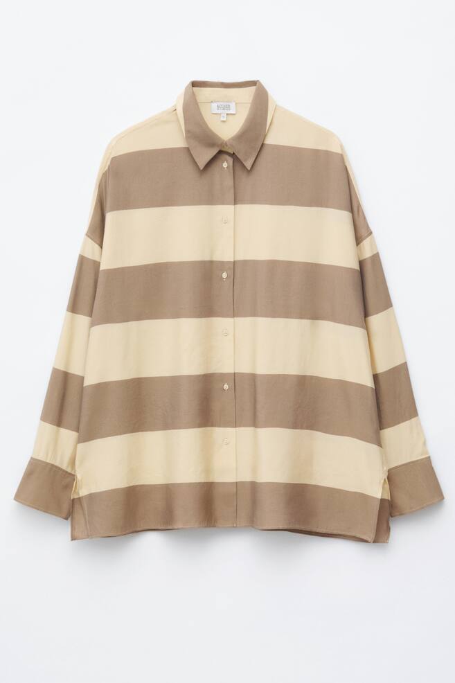 Una camisa de corte holgado se presenta de frente, con amplias rayas horizontales en tonos beige claro y marrón medio alternados. Está diseñada con un cuello en punta, una tapeta completa de botones con botones de color claro, mangas largas con puños de un solo botón y un dobladillo recto con aberturas laterales. - 1