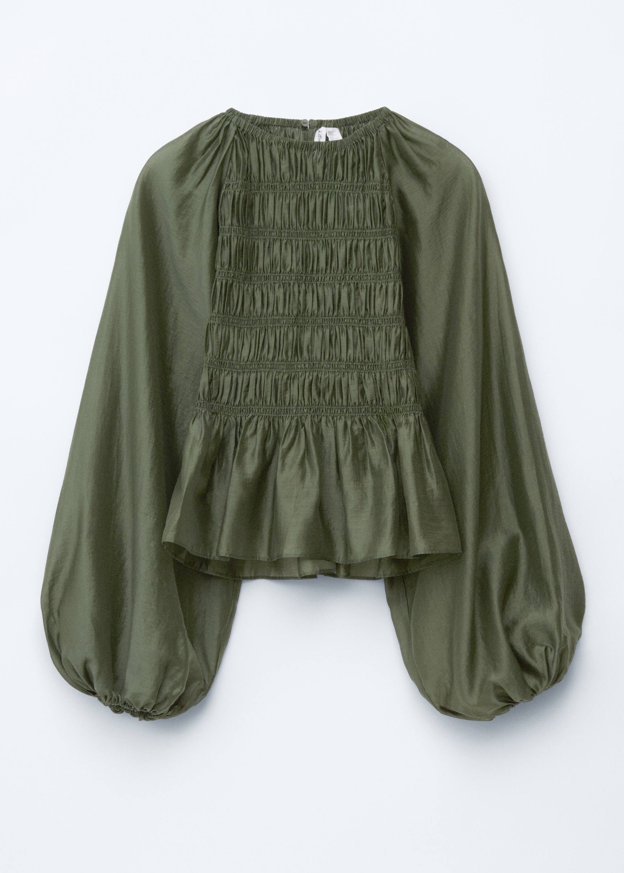 View larger image: A front view of an olive green blouse, crafted from a lustrous weave, is showcasing a round, elasticated neckline. Its bodice is featuring prominent smocking that is flaring into a peplum hemline, and raglan balloon sleeves are extending and are ending in elasticated cuffs.
