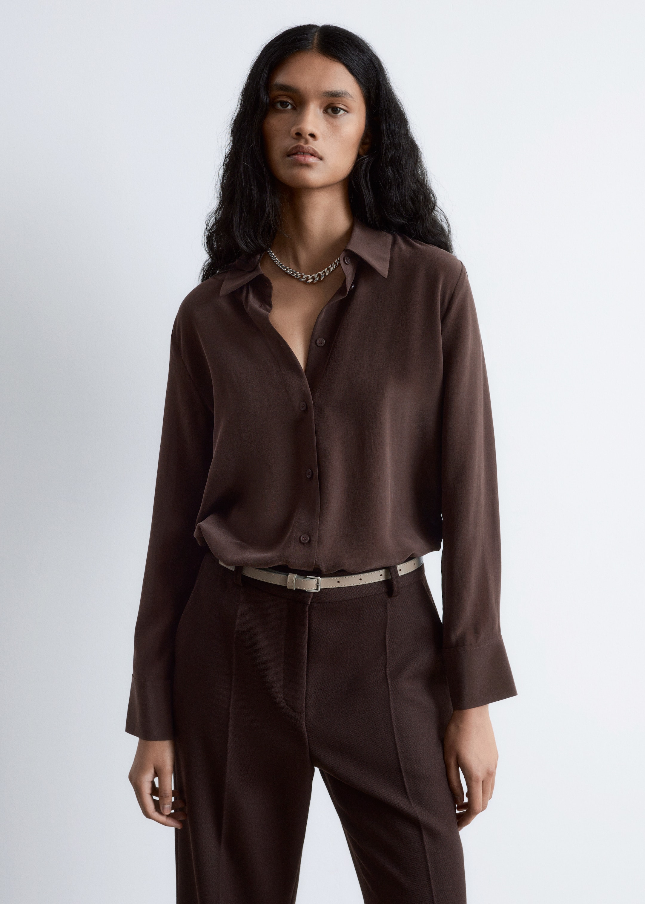 Visualizza immagine più grande: Una camicia marrone scuro a maniche lunghe con colletto a punta è presentata dal davanti, parzialmente infilata in pantaloni su misura marrone scuro abbinati. Una sottile cintura beige chiaro con fibbia rettangolare stringe i pantaloni in vita.