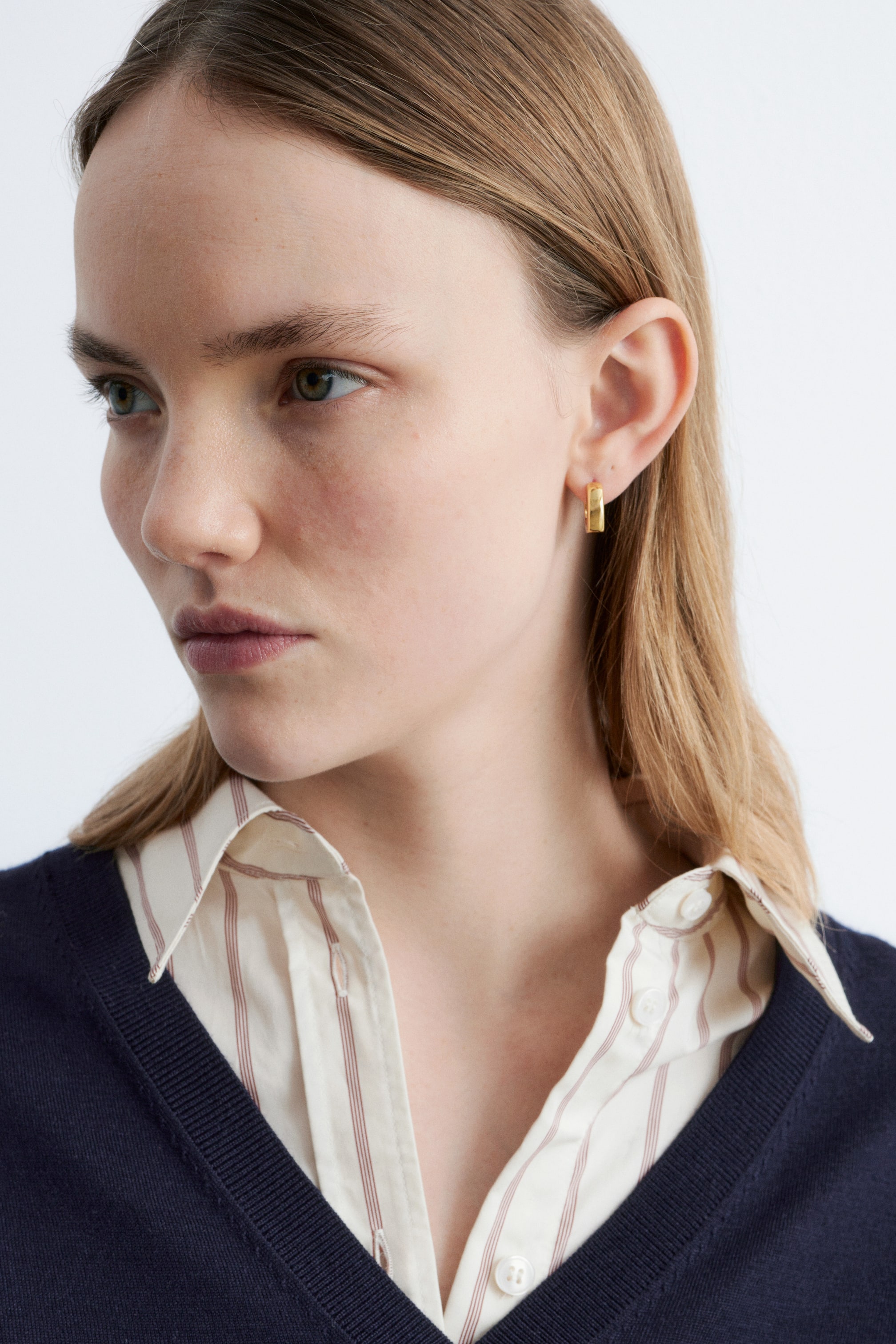 View larger image: A gold-toned, rectangular hoop earring is being worn on the earlobe, with its flat side facing forward.