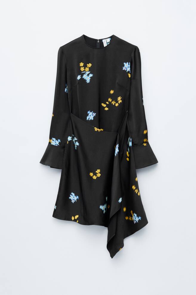 Ein schwarzes Kleid zeigt einen runden Ausschnitt, lange Ärmel mit ausgestellten Manschetten und verstreute gelbe und blaue Blumenmotive, die von vorne betrachtet werden. Es verfügt über ein vorderes Überlappungspanel, das einen asymmetrischen Saum erzeugt. - 1