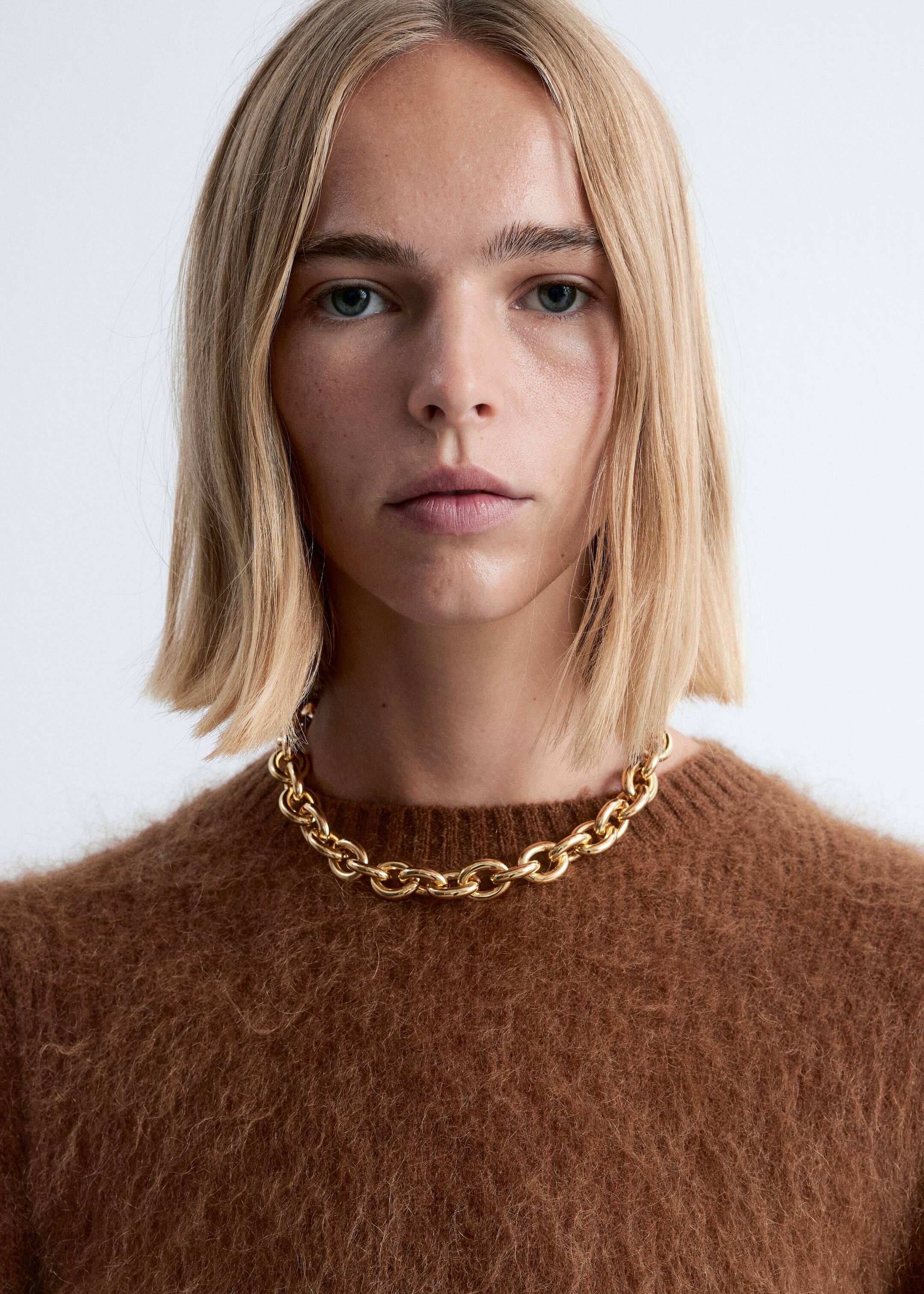 View larger image: A gold-tone chunky chain necklace, featuring large oval links, is being worn over a brown fuzzy crew-neck sweater.