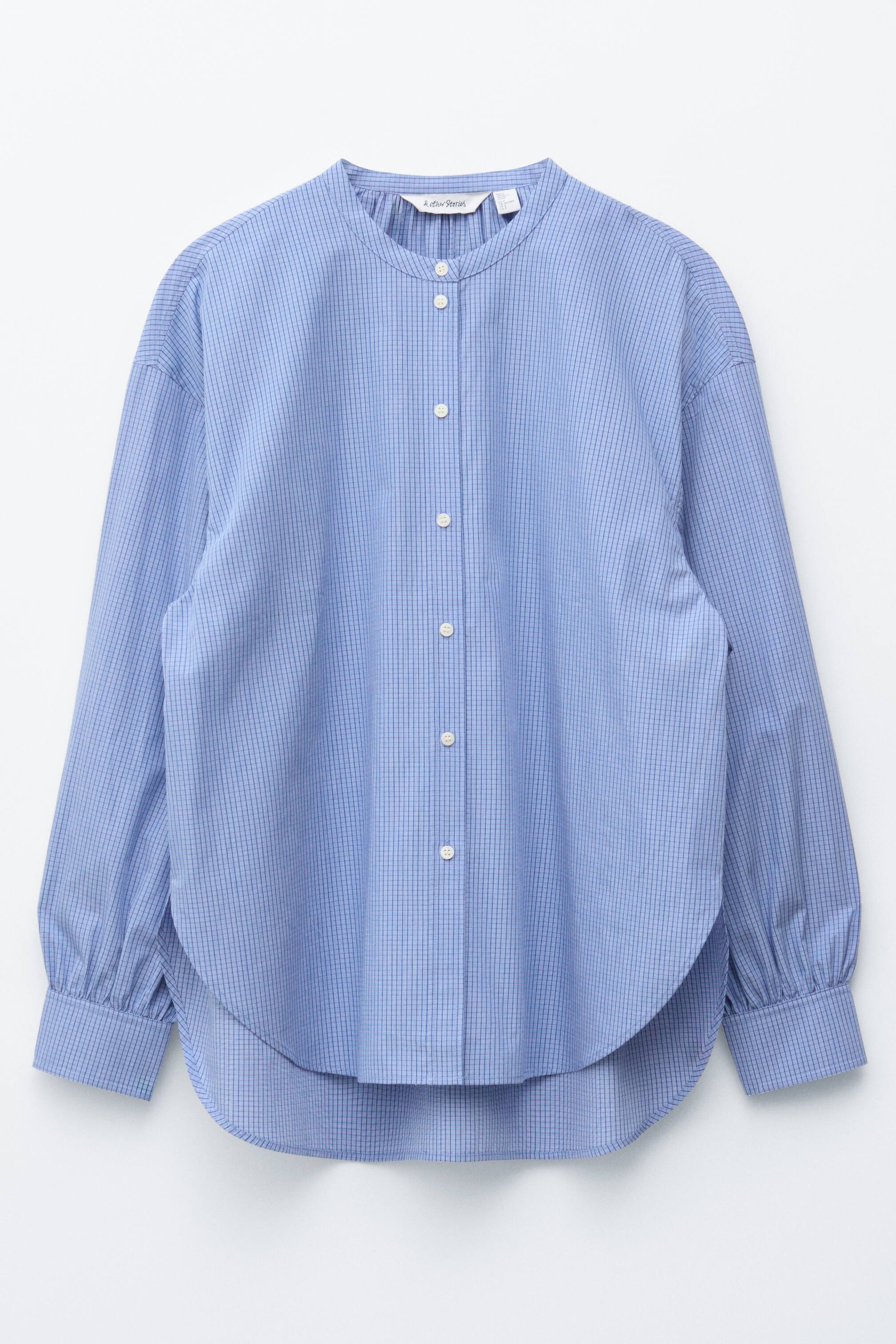 Grotere afbeelding bekijken: Een blauwe oversized shirt met een subtiel ruitpatroon wordt van de VOORKANT getoond, met een bandkraag, een voorste knoopsluiting met witte knopen, verlaagde schouders, lange mouwen met knoopmanchetten en een afgeronde zoom.