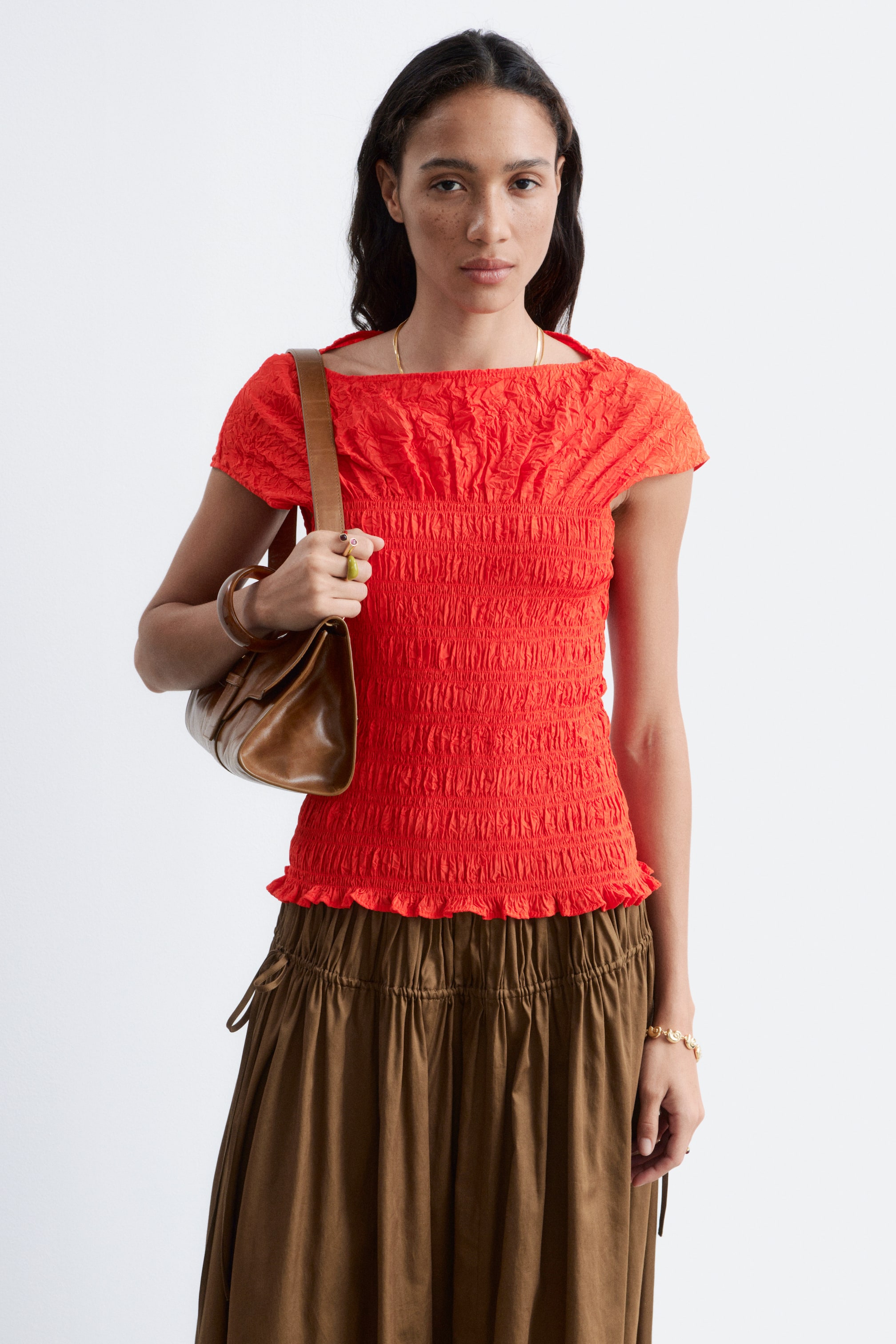 Agrandir l'image: Un haut rouge vif présente un décolleté carré et de courtes manches à capuchon. Le haut affiche un tissu texturé et froncé sur la poitrine, et le corps est fortement plissé, se terminant par un ourlet subtilement volanté.