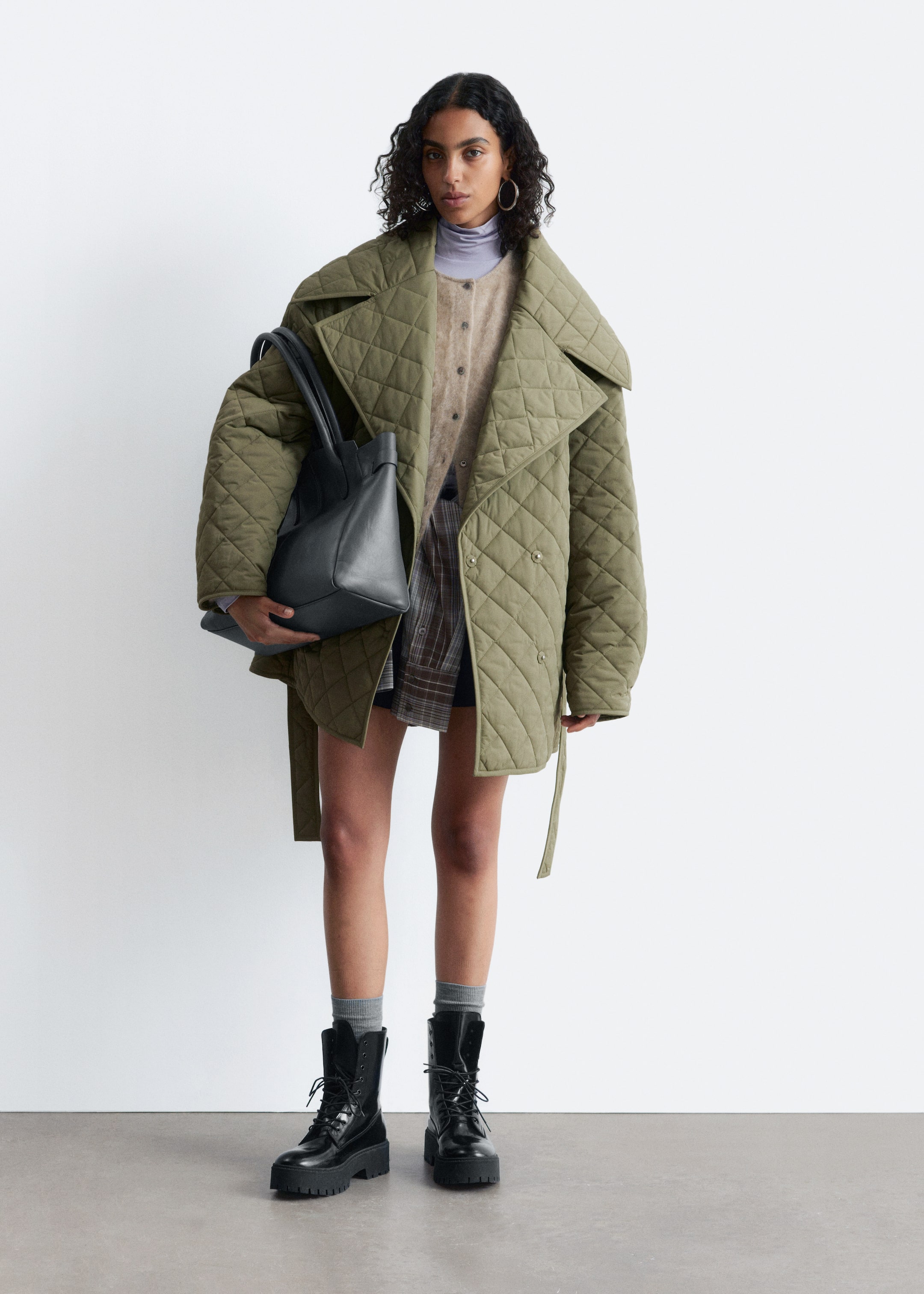 View larger image: An olive green quilted jacket is being presented from the front, draped open over the shoulders. It is featuring a diamond quilt pattern, wide lapels, a double-breasted front with two visible buttons, and matching fabric ties hanging loosely at the sides.
