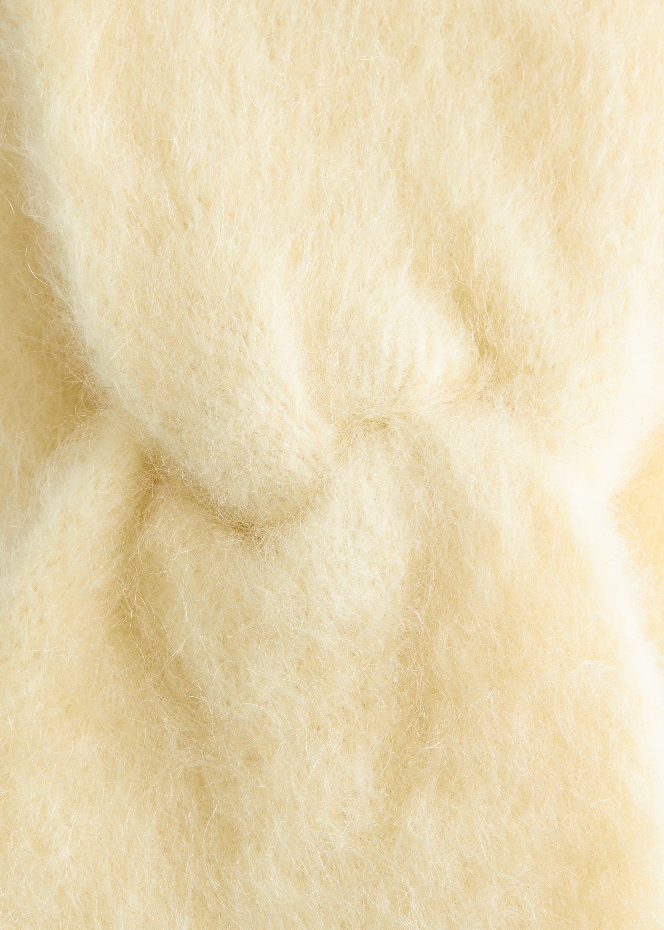 Grösseres Bild ansehen: Das Mohair-Mix Stirnband mit Twist-Front wird im Nahaufnahme seiner Stoffbeschaffenheit präsentiert, wobei eine weiche, flauschige Textur mit langen, feinen, blassgelben Fasern zu sehen ist, die subtile Variationen in der Tiefe aufweisen.