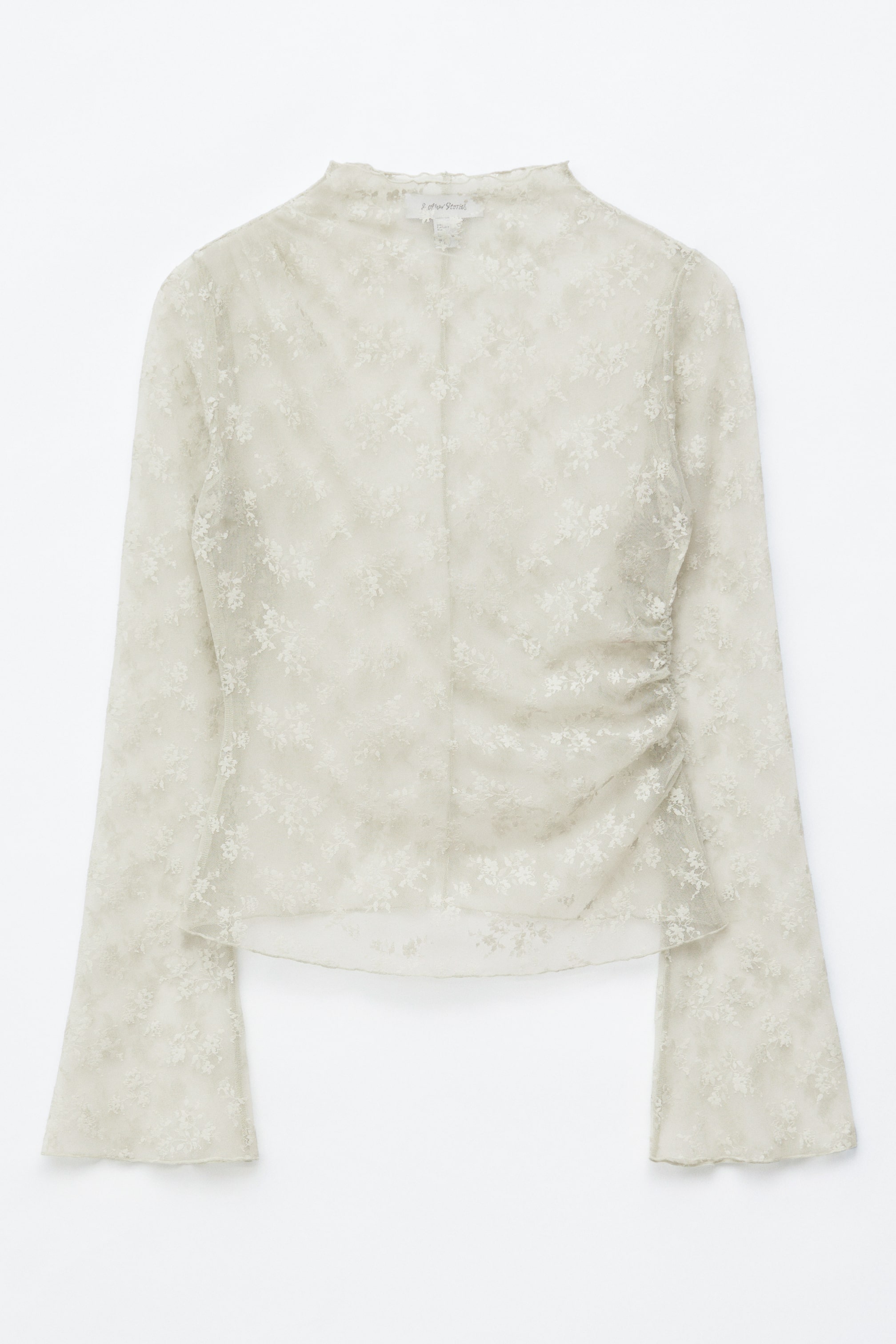 Agrandir l'image: Le haut est présenté à l'avant, confectionné en dentelle transparente de teinte claire avec un motif floral décoratif. Il est doté d'un col montant, de manches longues évasées et de fronces aux épaules et à la taille.