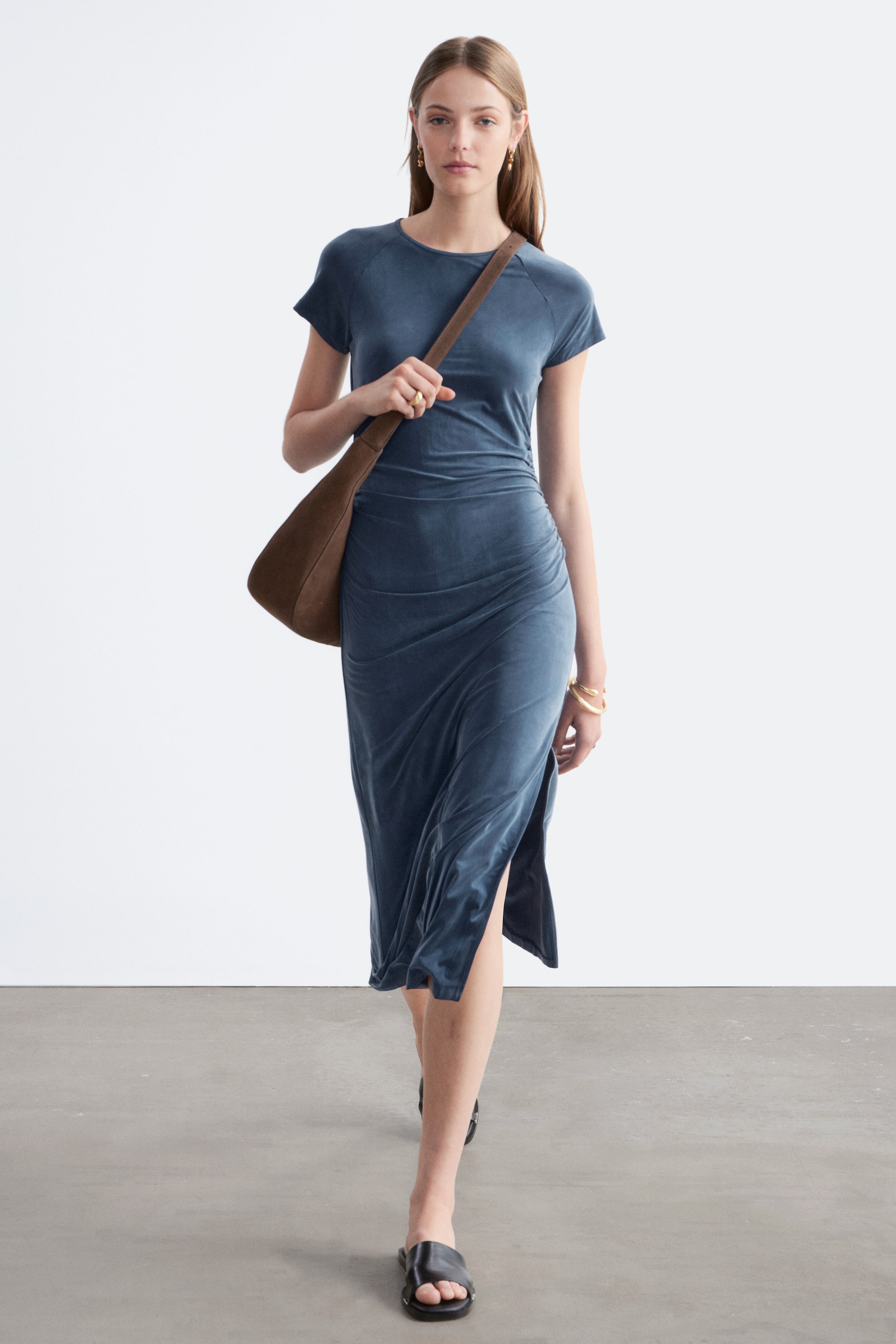 Agrandir l'image: Une robe midi en velours bleu profond avec des manches raglan courtes, un col rond et des détails froncés sur le côté droit, avec une fente haute visible sur le côté gauche.