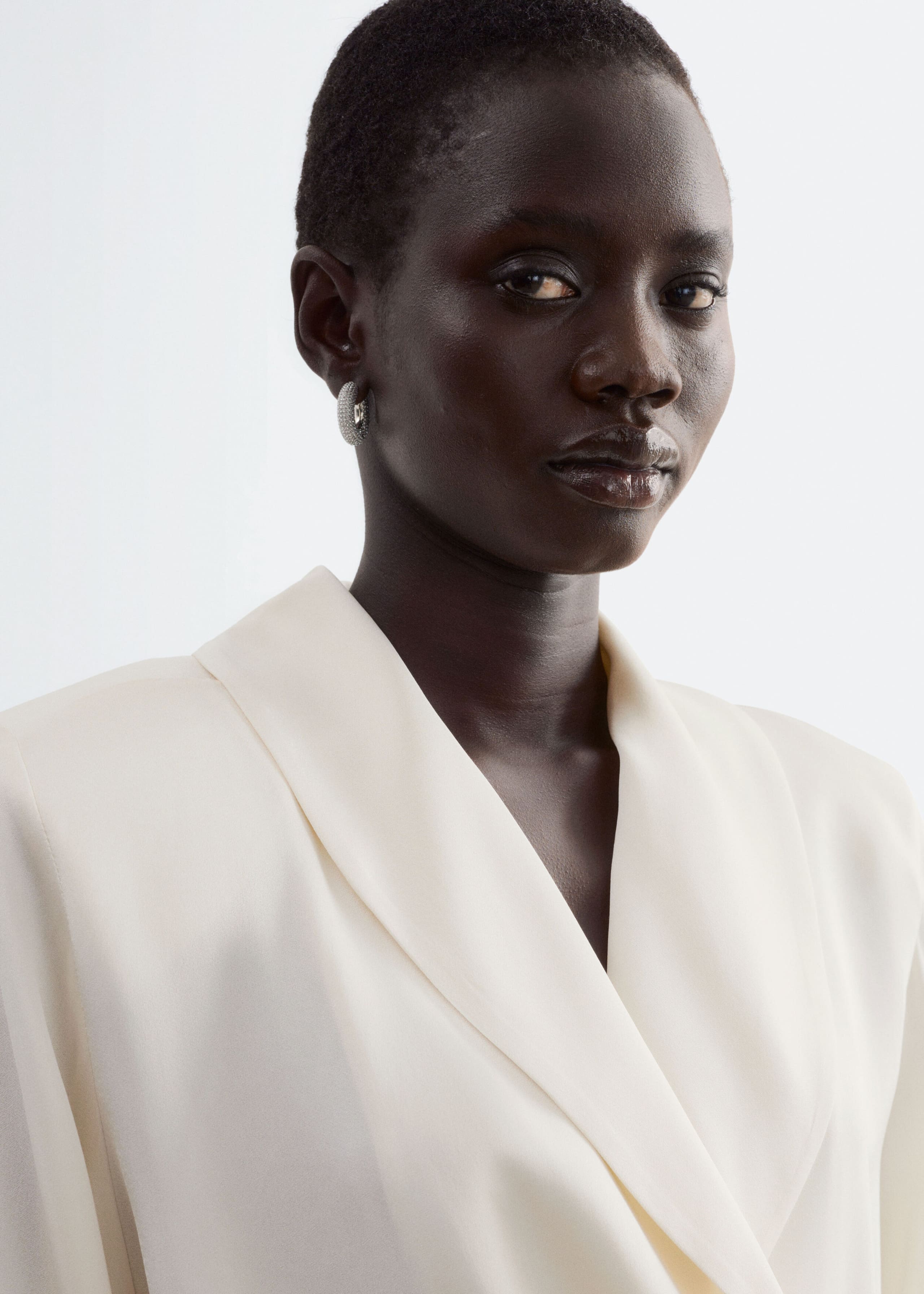 La modella indossa una blusa avvolgente color crema con un morbido colletto a scialle. La vista ravvicinata mette in risalto lo scollo incrociato e drappeggiato del tessuto liscio.