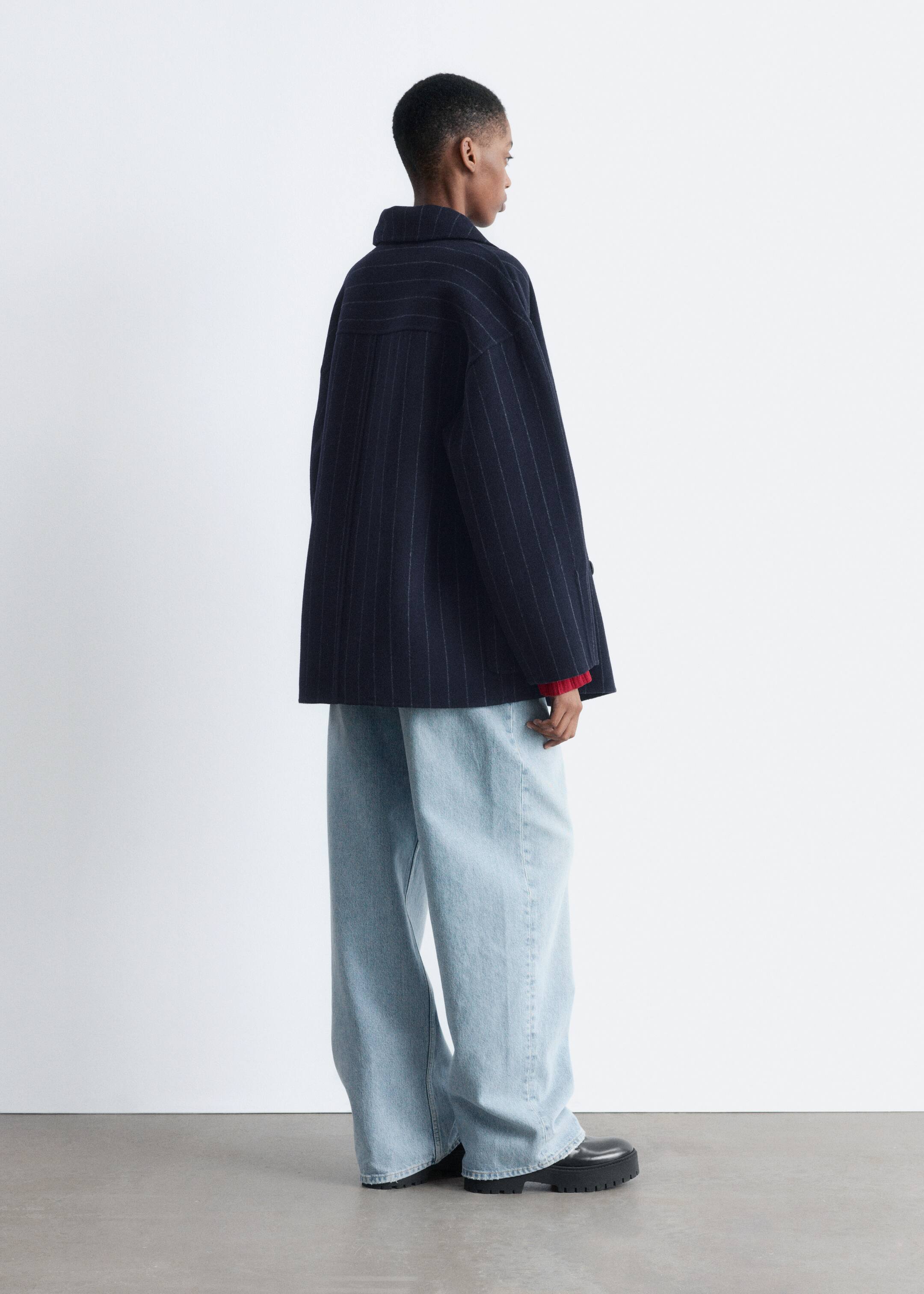 Visualizza immagine più grande: La modella indossa una giacca a righe navy, caratterizzata da una silhouette rilassata a bozzolo e un collo in piedi, con sotto un indumento rosso visibilmente stratificato.
