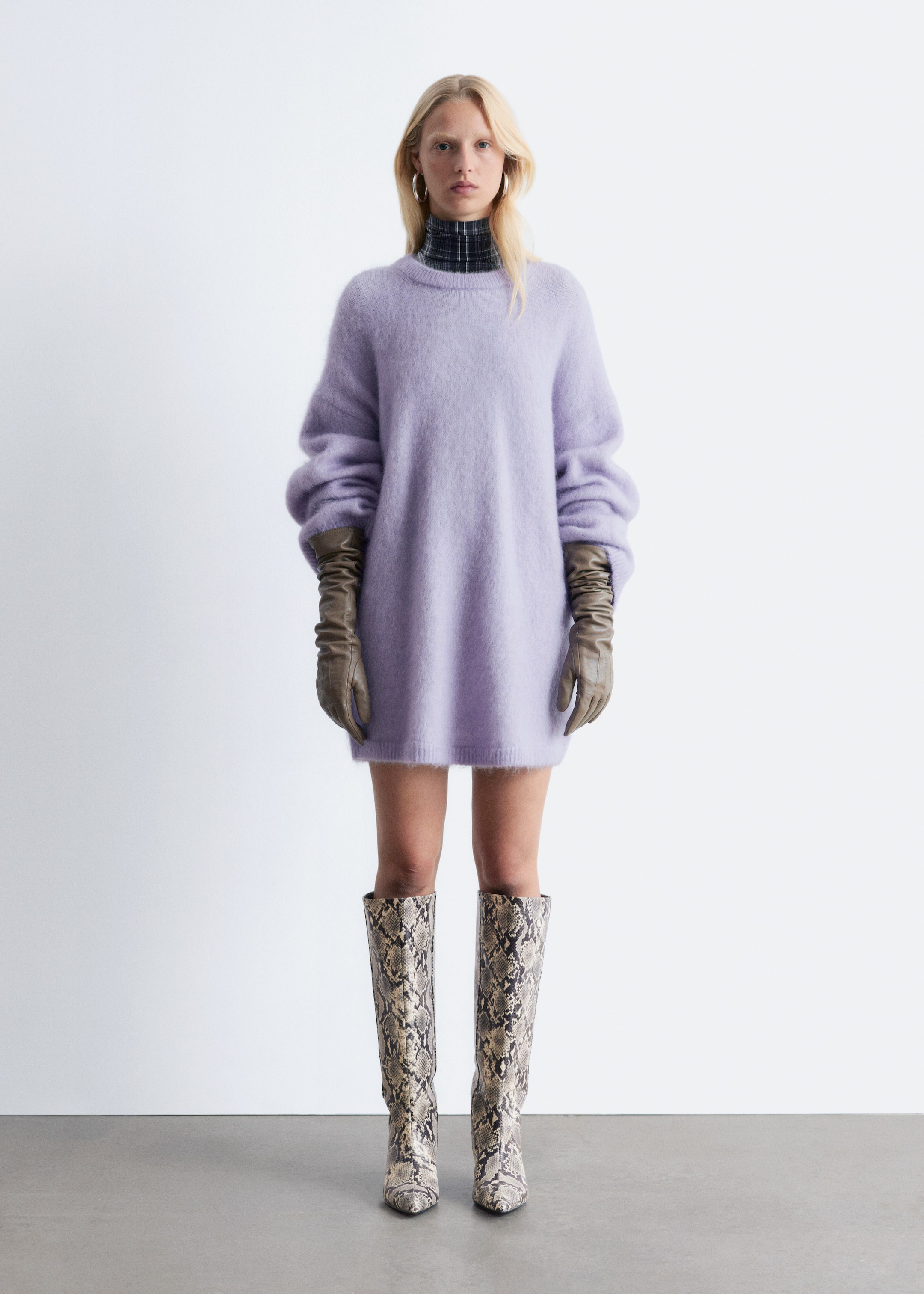 Grösseres Bild ansehen: Ein hellviolettes, flauschiges, übergroßes Strickkleid wird frontal präsentiert, mit einem Rundhalsausschnitt und voluminösen langen Ärmeln. Darunter wird ein dunkler karierter Rollkragenpullover getragen, und lange olivfarbene Handschuhe bedecken die Arme und reichen über die Ärmel des Pullovers hinaus.