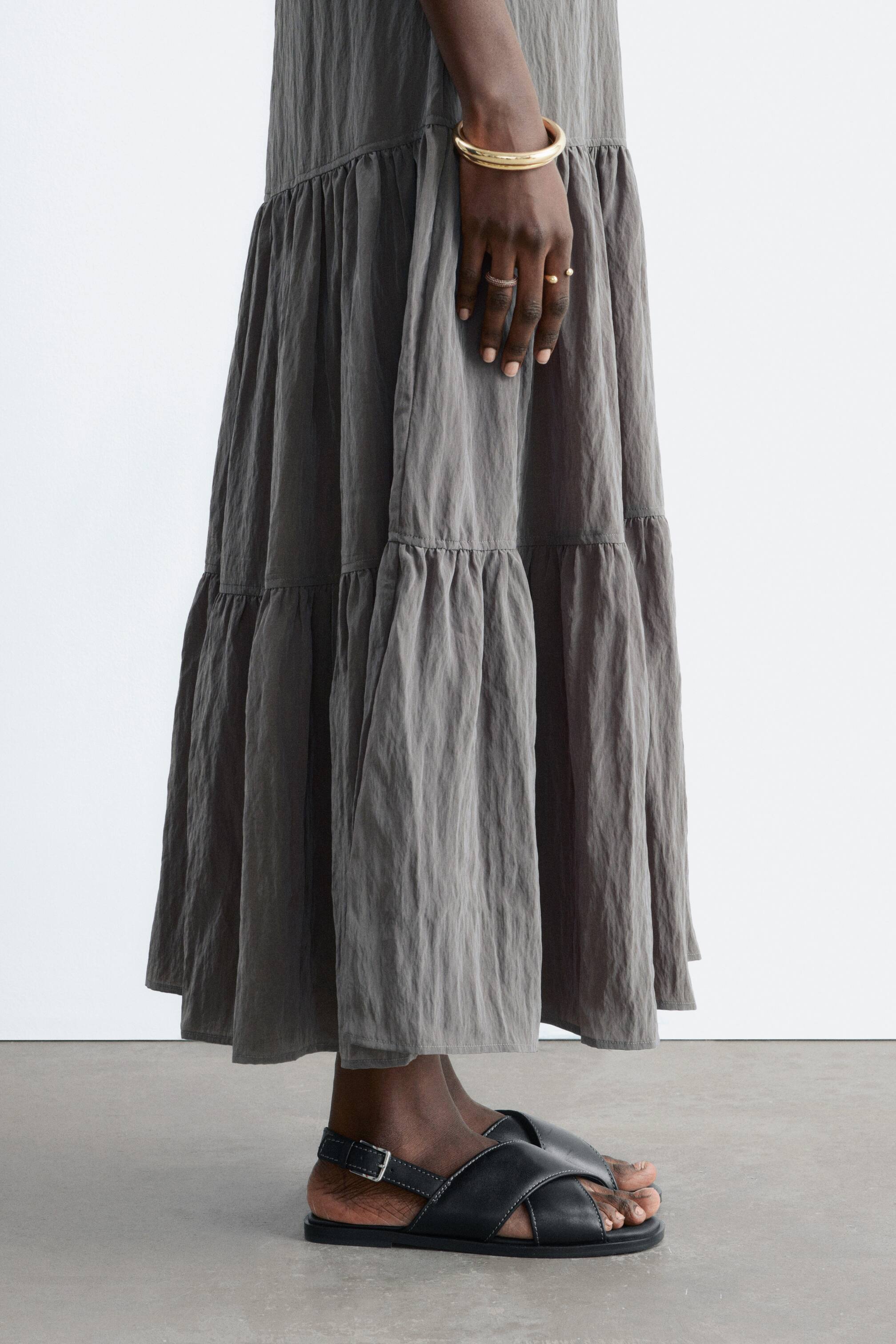 Ver imagen más grande: Una prenda de color gris oscuro con capas cae hacia abajo, con múltiples costuras fruncidas y una textura arrugada.