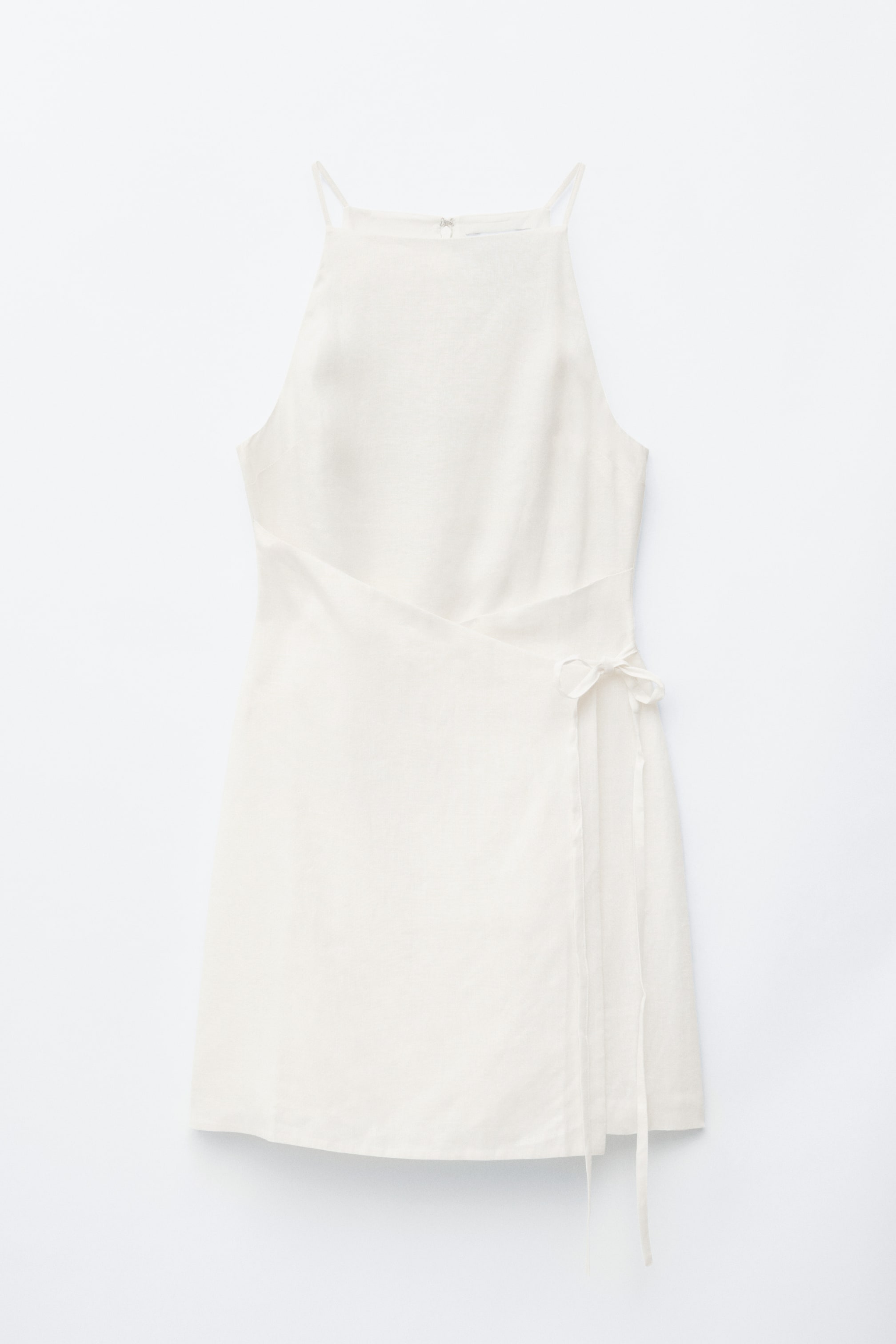 Agrandir l'image: Une robe courte blanc cassé est présentée à plat, face avant, mettant en valeur un décolleté carré haut et de fines bretelles. Elle présente un design portefeuille à l'avant, maintenu par de fines bandes nouées en un nœud sur le côté droit.