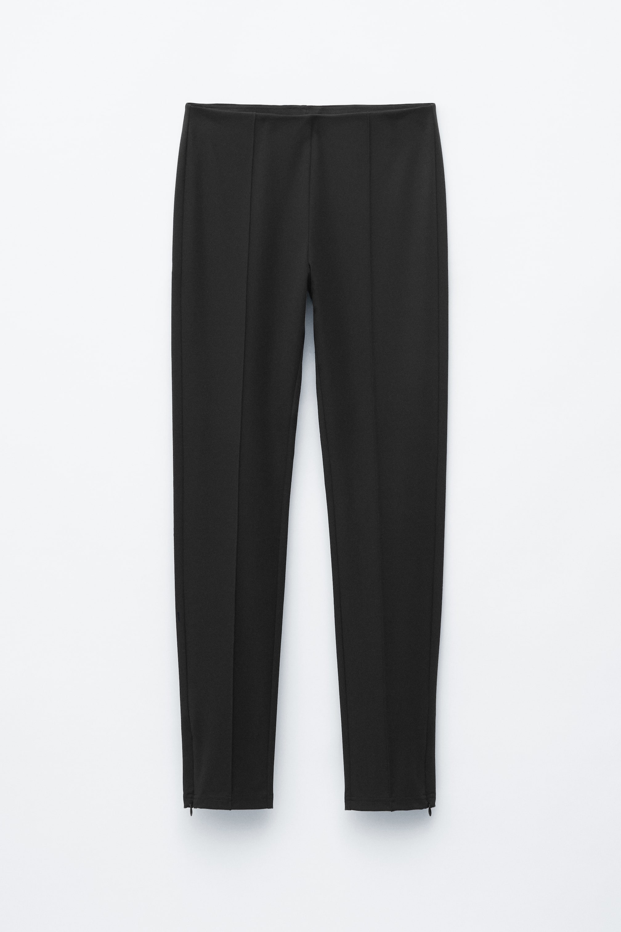 Nagyobb kép megtekintése: A fekete nadrágok laposan fekszenek, elölről láthatók. Simán elasztikus derékpánttal rendelkeznek, függőleges varratok futnak végig a lábak elején, és kis cipzárak találhatók a külső bokaszegélyeknél.