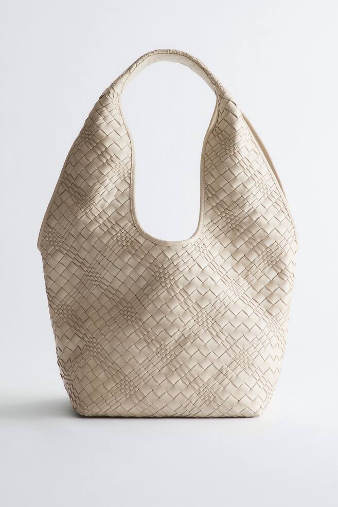 Cabas en cuir tressé. Ce cabas beige clair présente un motif en cuir tissé sur l'ensemble de son corps souple et décontracté, avec une poignée supérieure intégrée. - 1